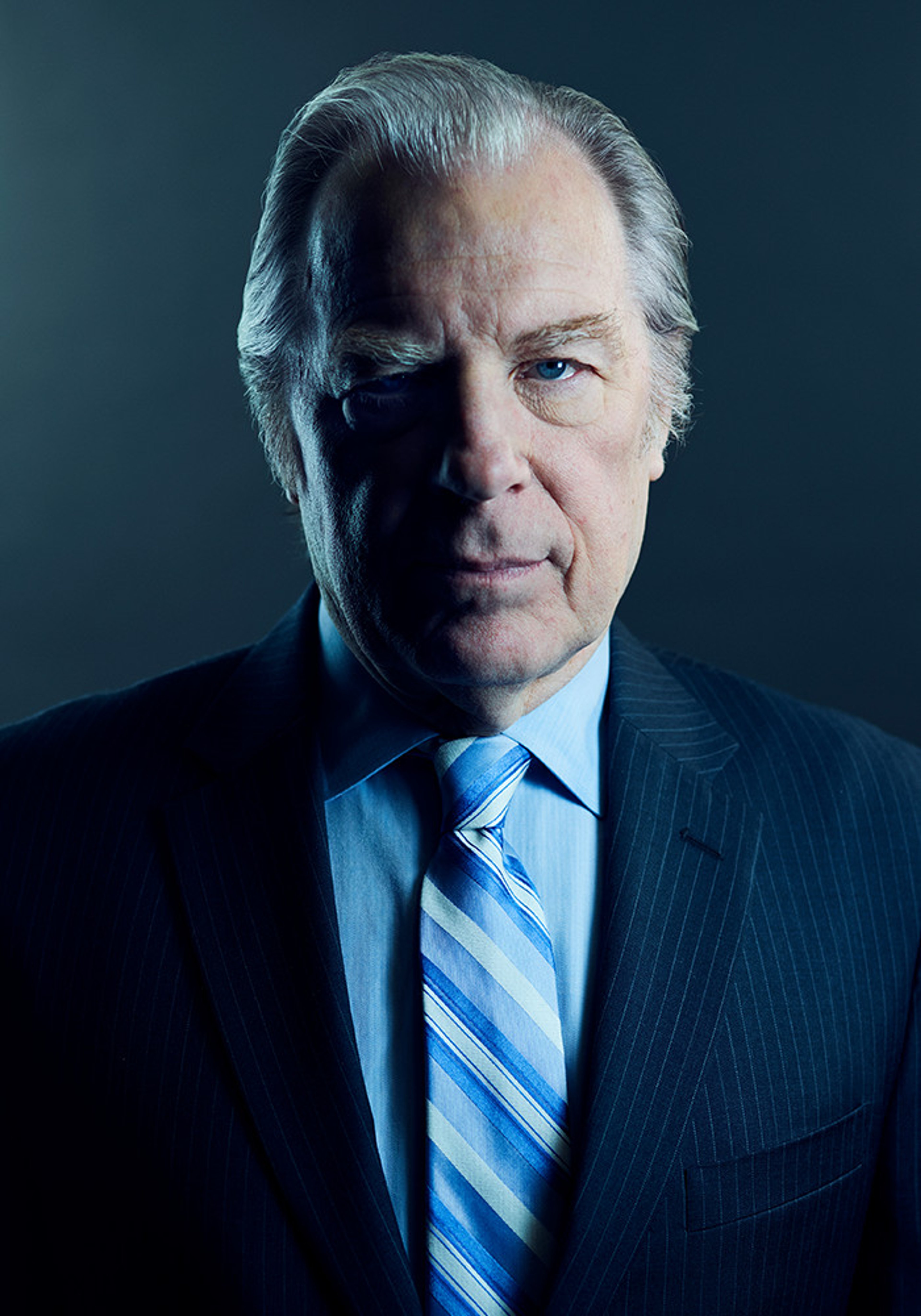 A middle-aged man in a blue suit and tie with a serious expression