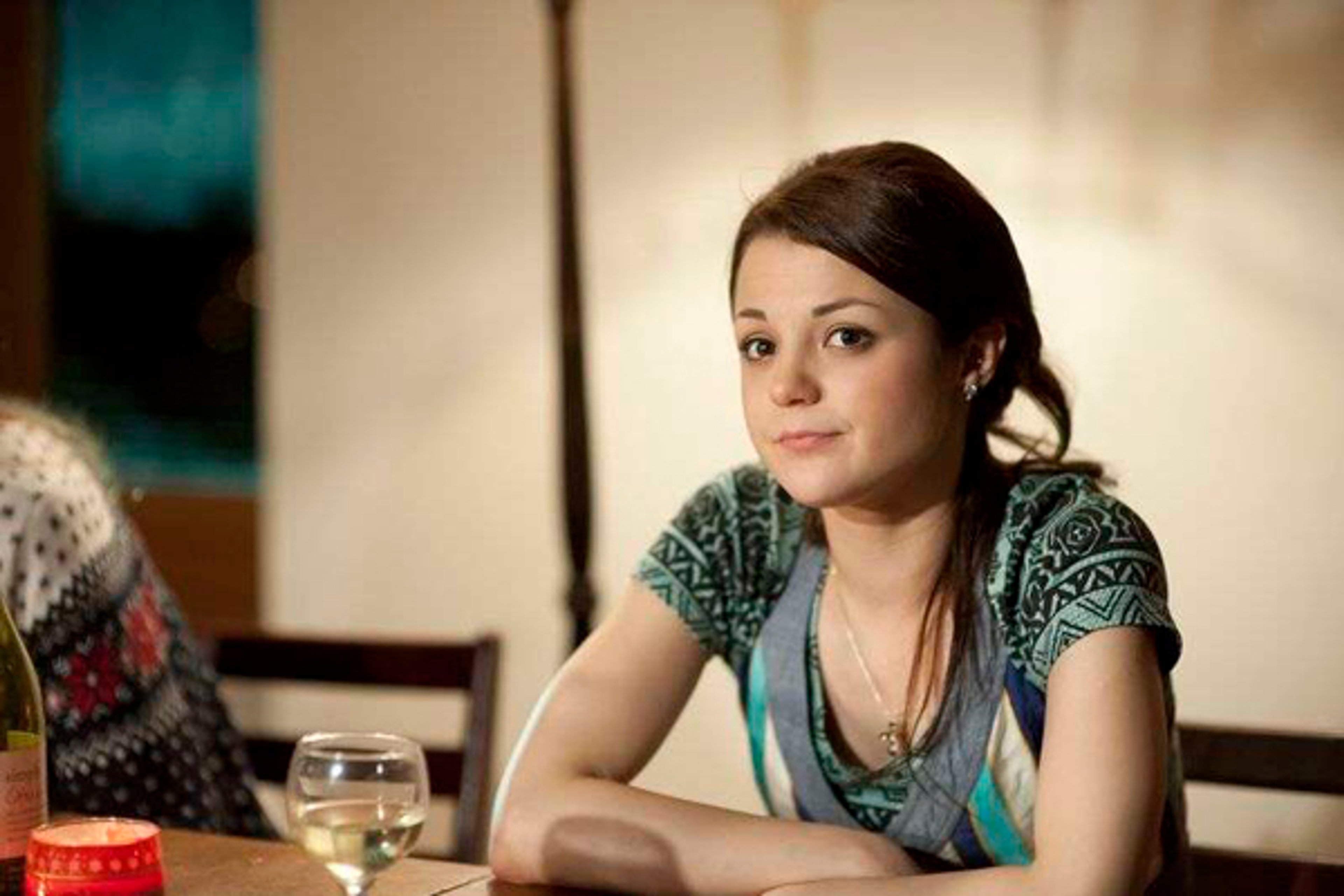 A young woman with dark hair sitting at a table, looking at the camera.