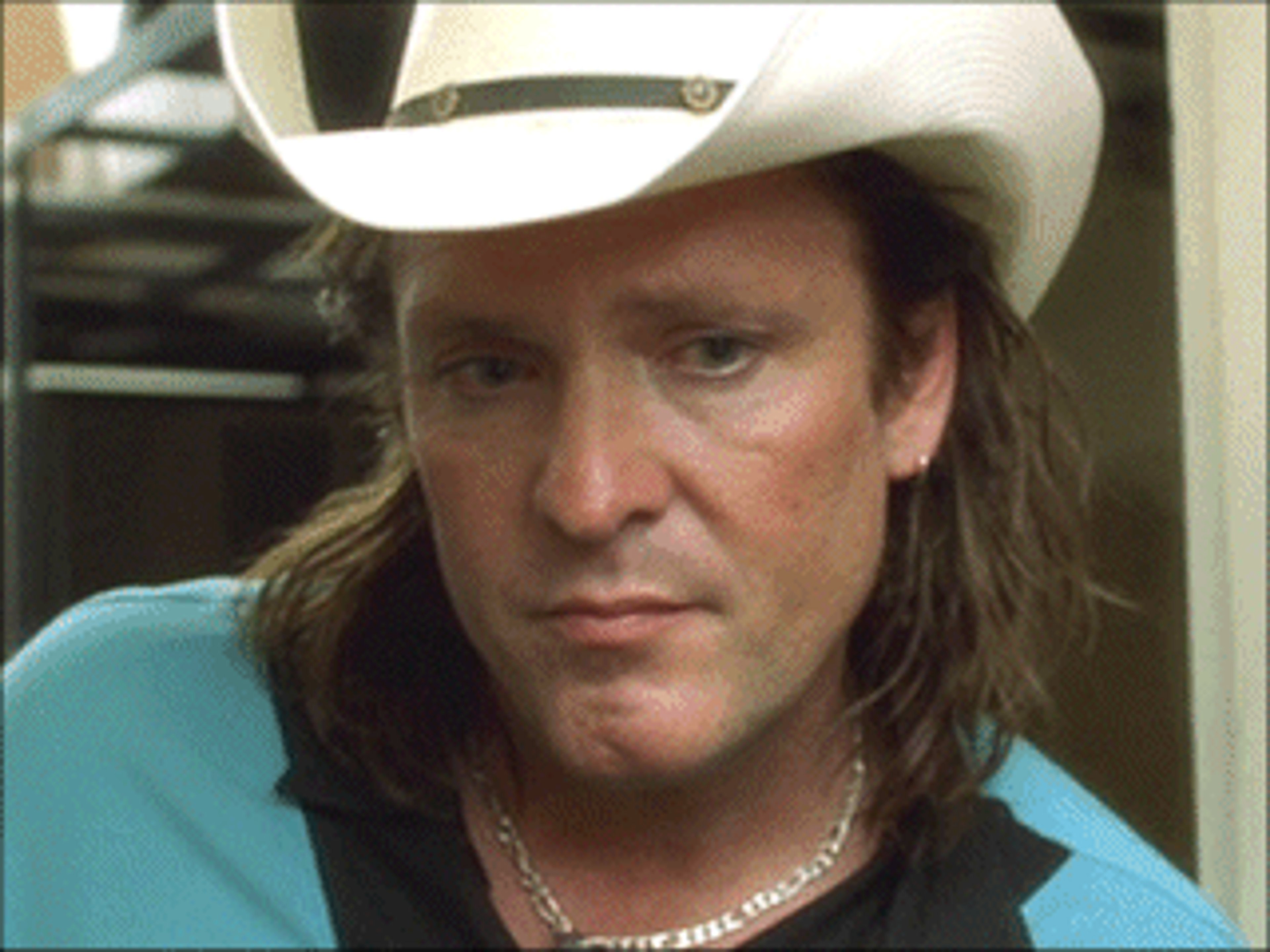 A middle-aged man with long hair and a mustache wearing a cowboy hat and a turquoise shirt
