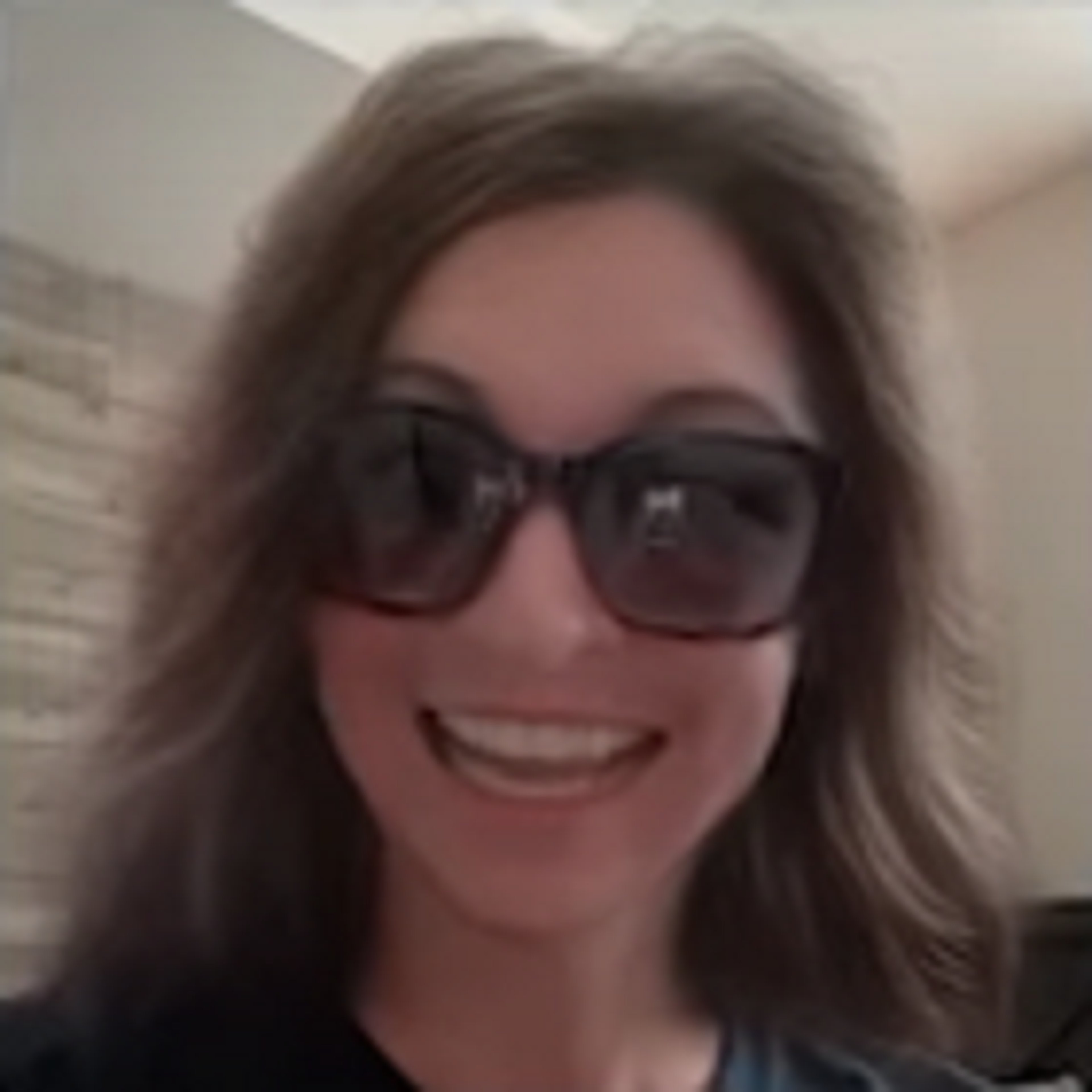 A smiling woman with long brown hair wearing sunglasses