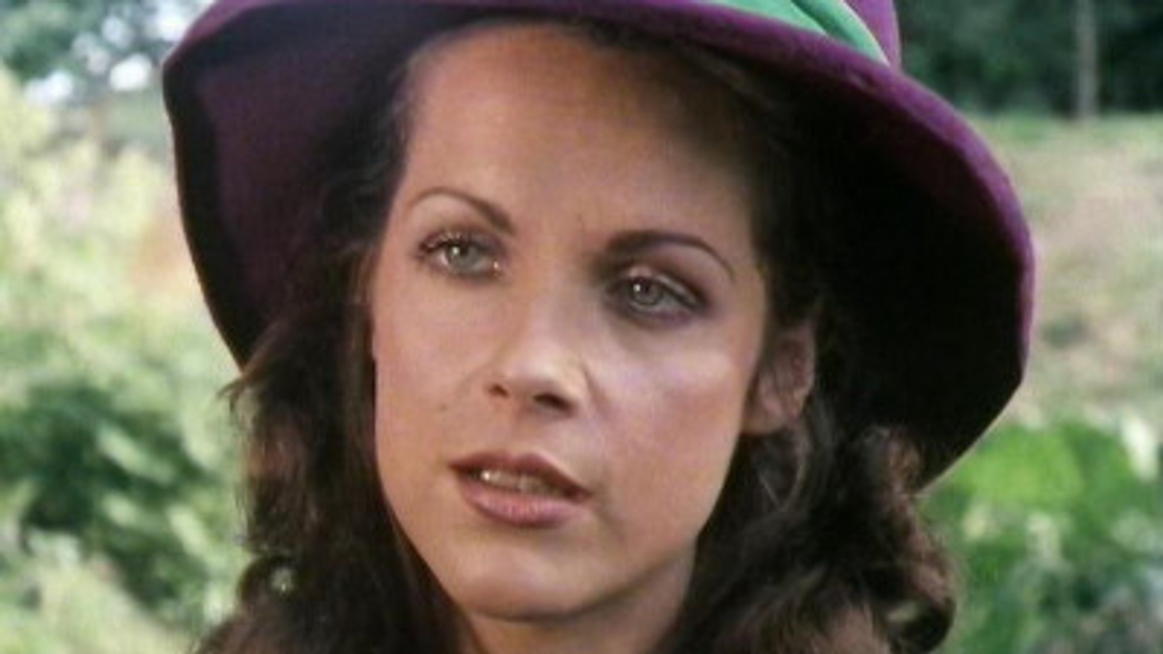 A woman with curly brown hair wearing a purple hat