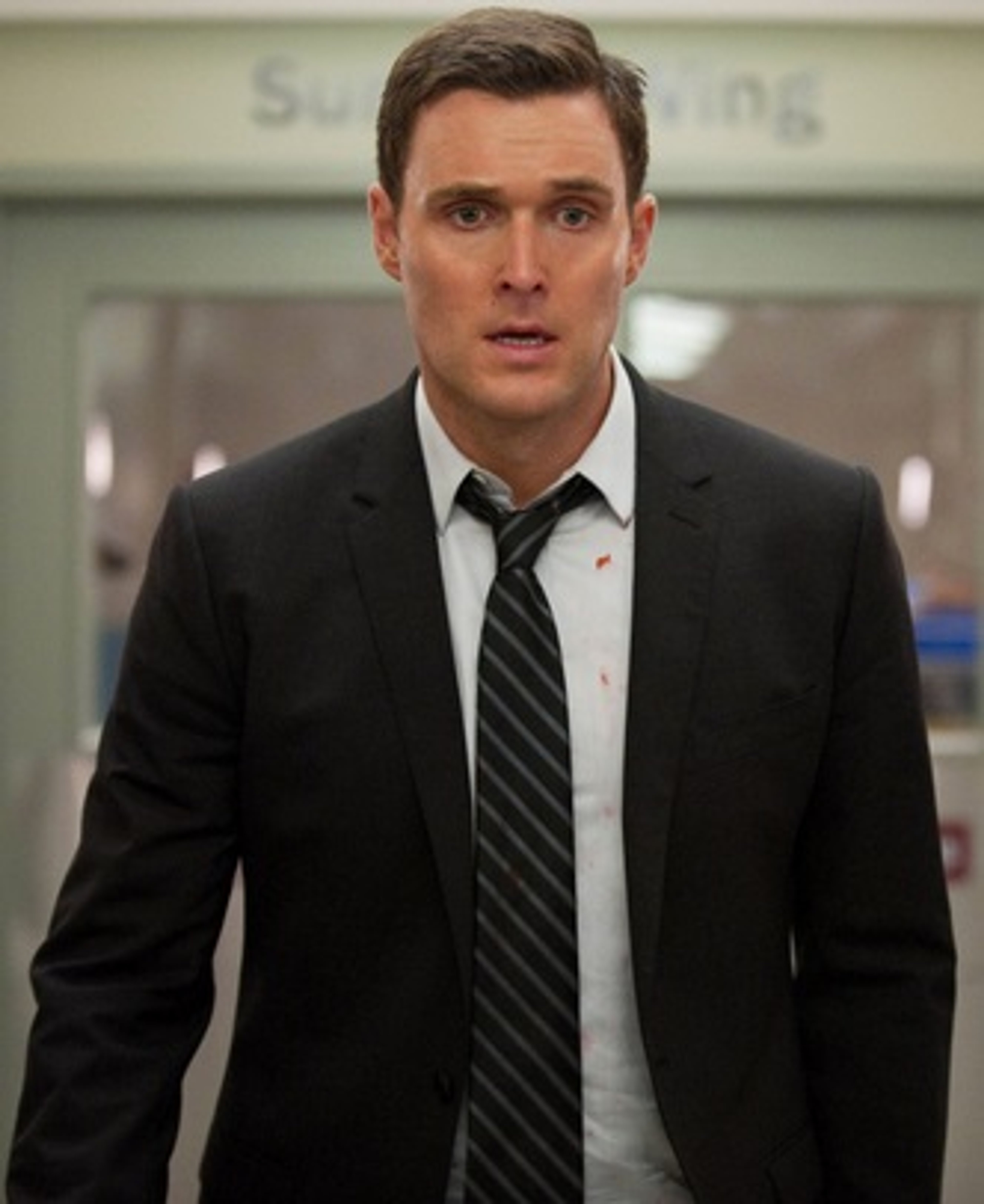 A man in a black suit and tie with a serious expression