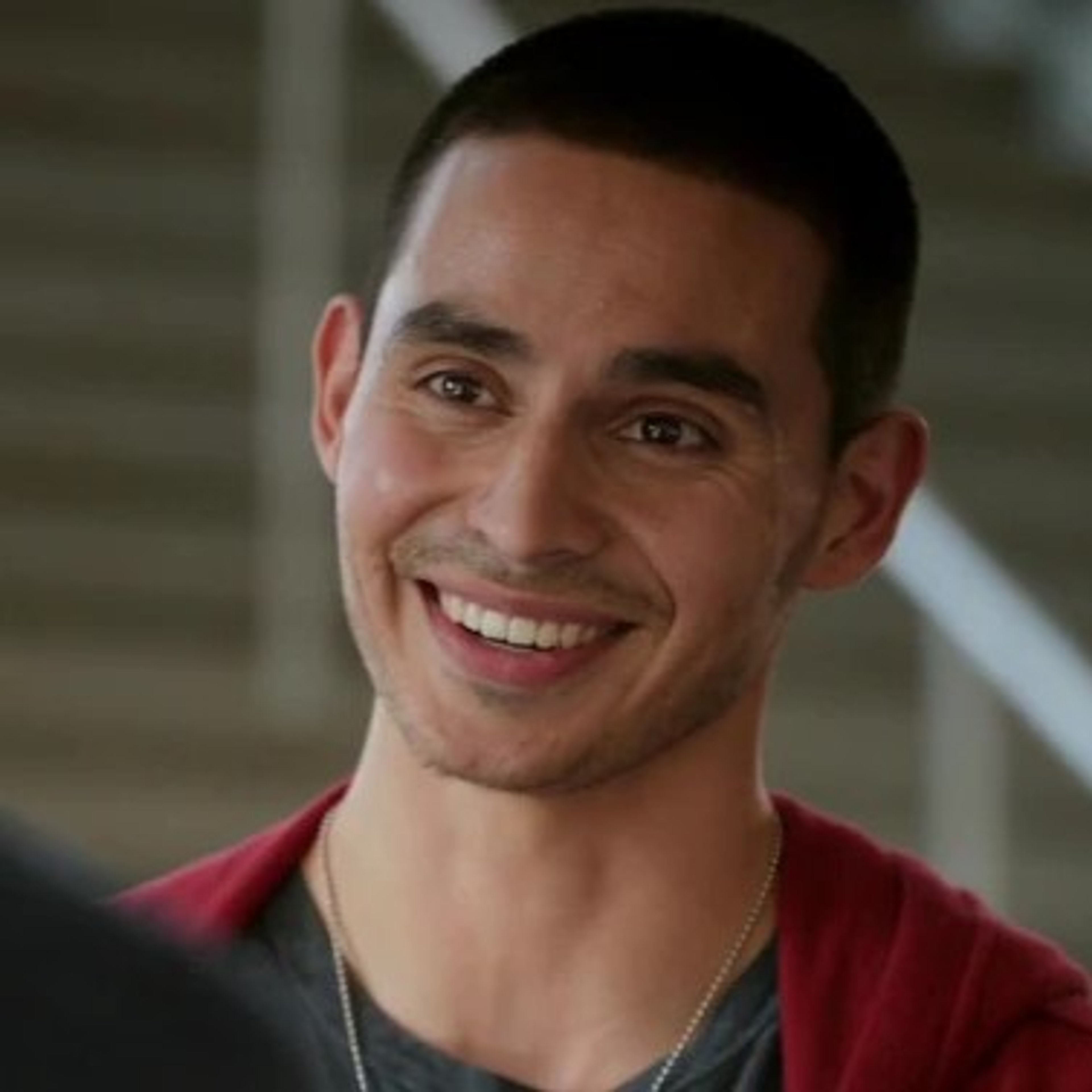 A smiling man with short dark hair wearing a red shirt