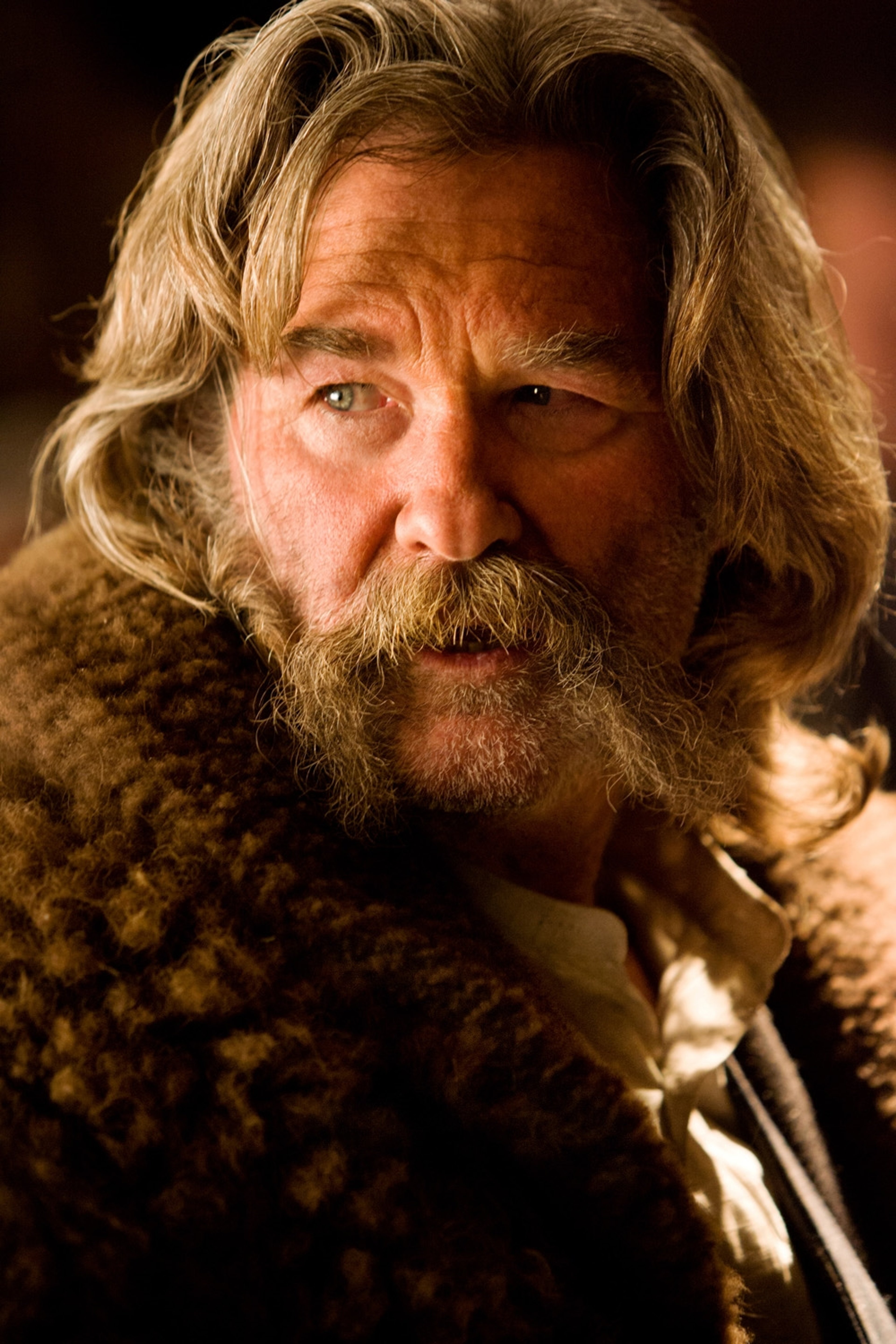 A grizzled, older man with a long beard and weathered face, wearing a fur-lined coat