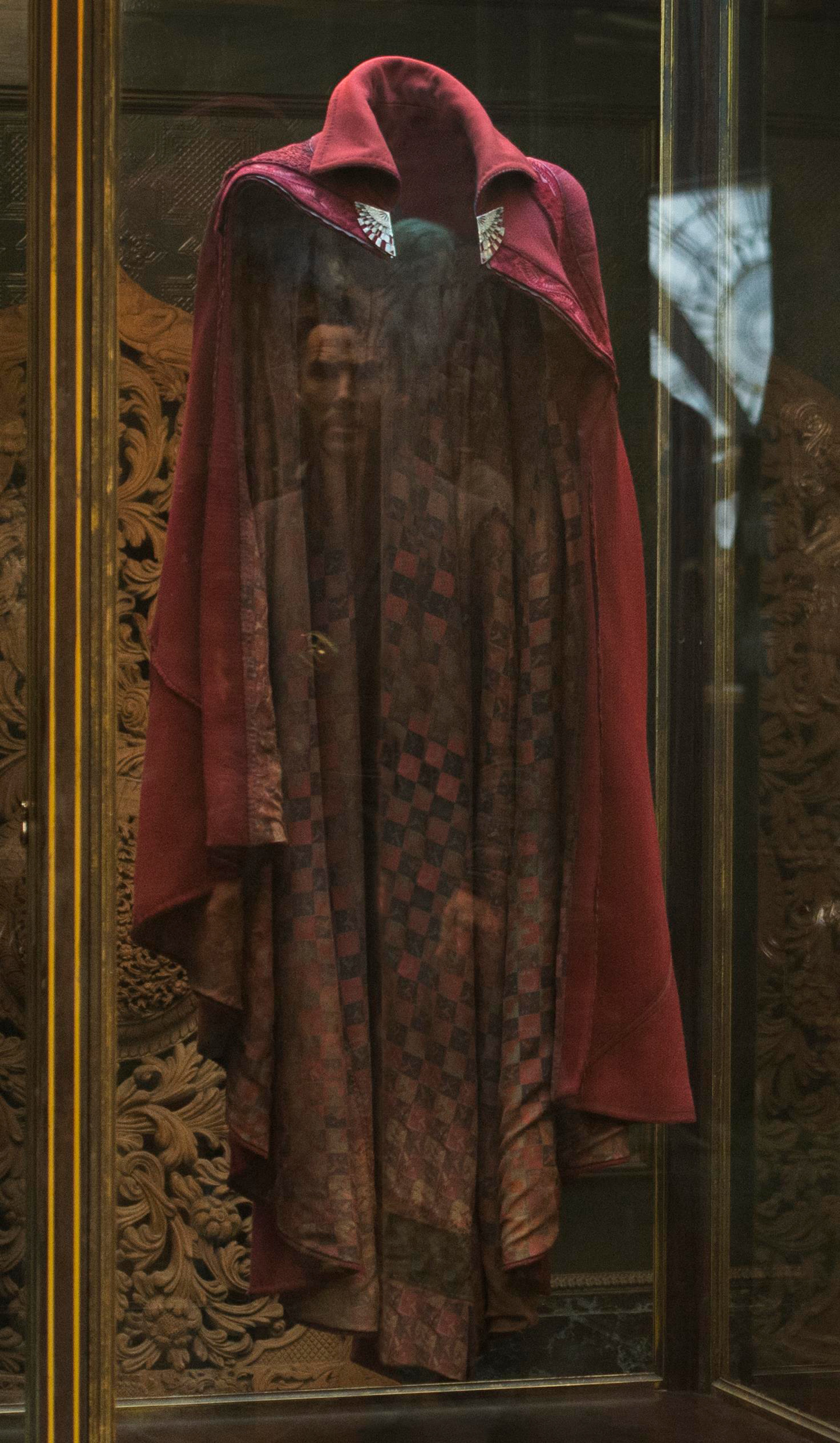 A person wearing a red hooded cloak in a dimly lit, ornate interior