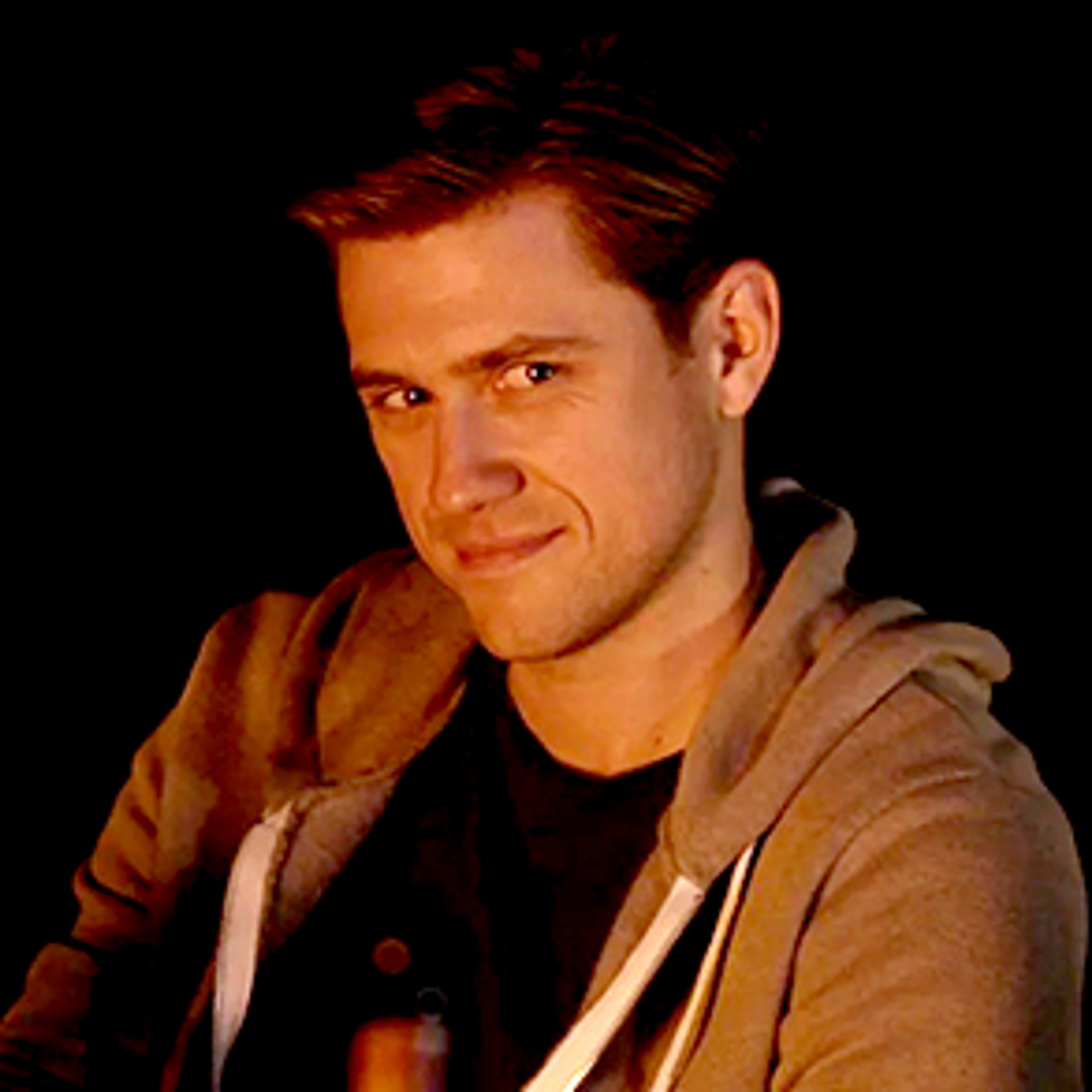 A serious-looking young man with short brown hair wearing a dark jacket