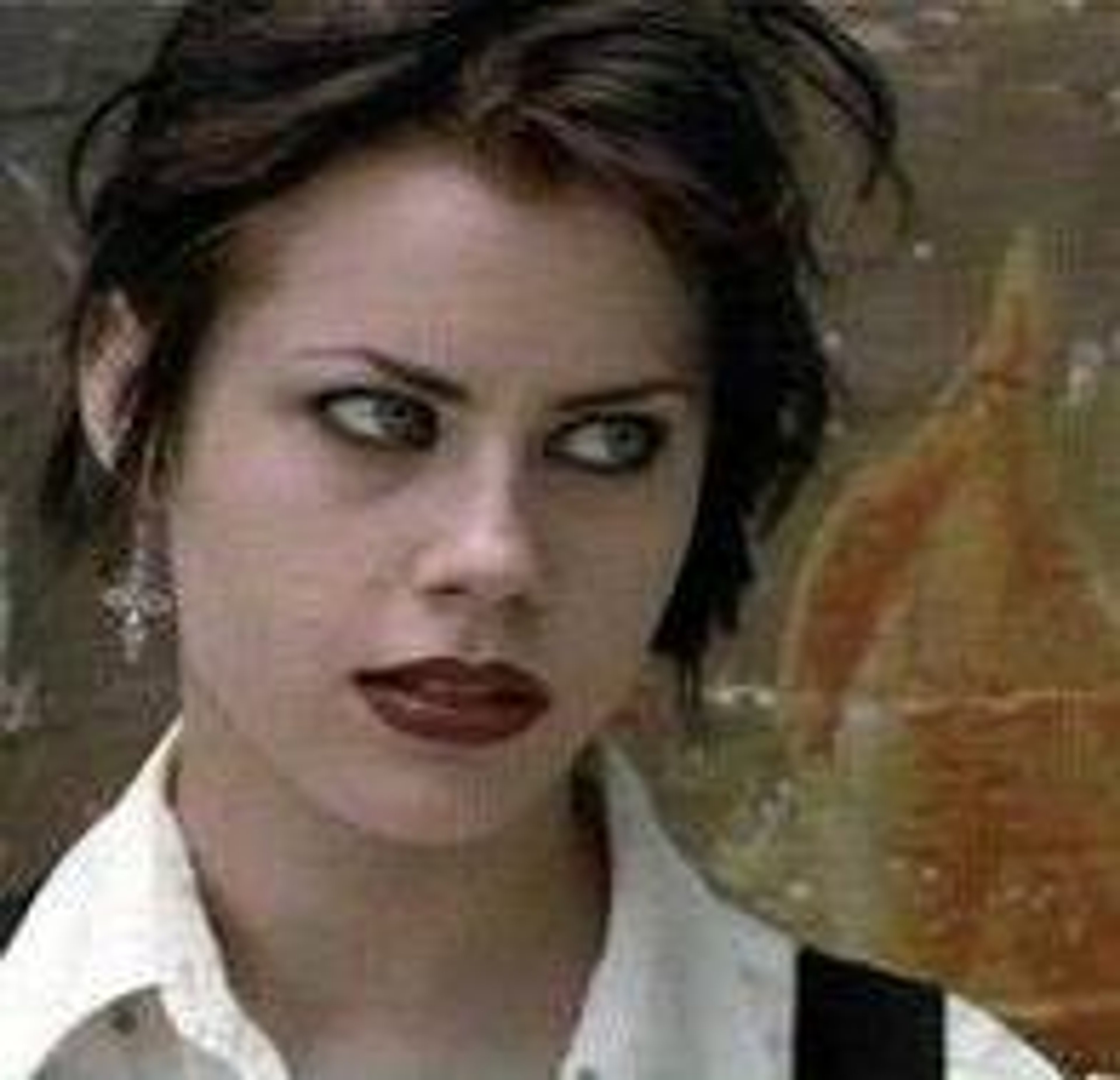 A young woman with dark hair and intense eyes, wearing a white collared shirt.