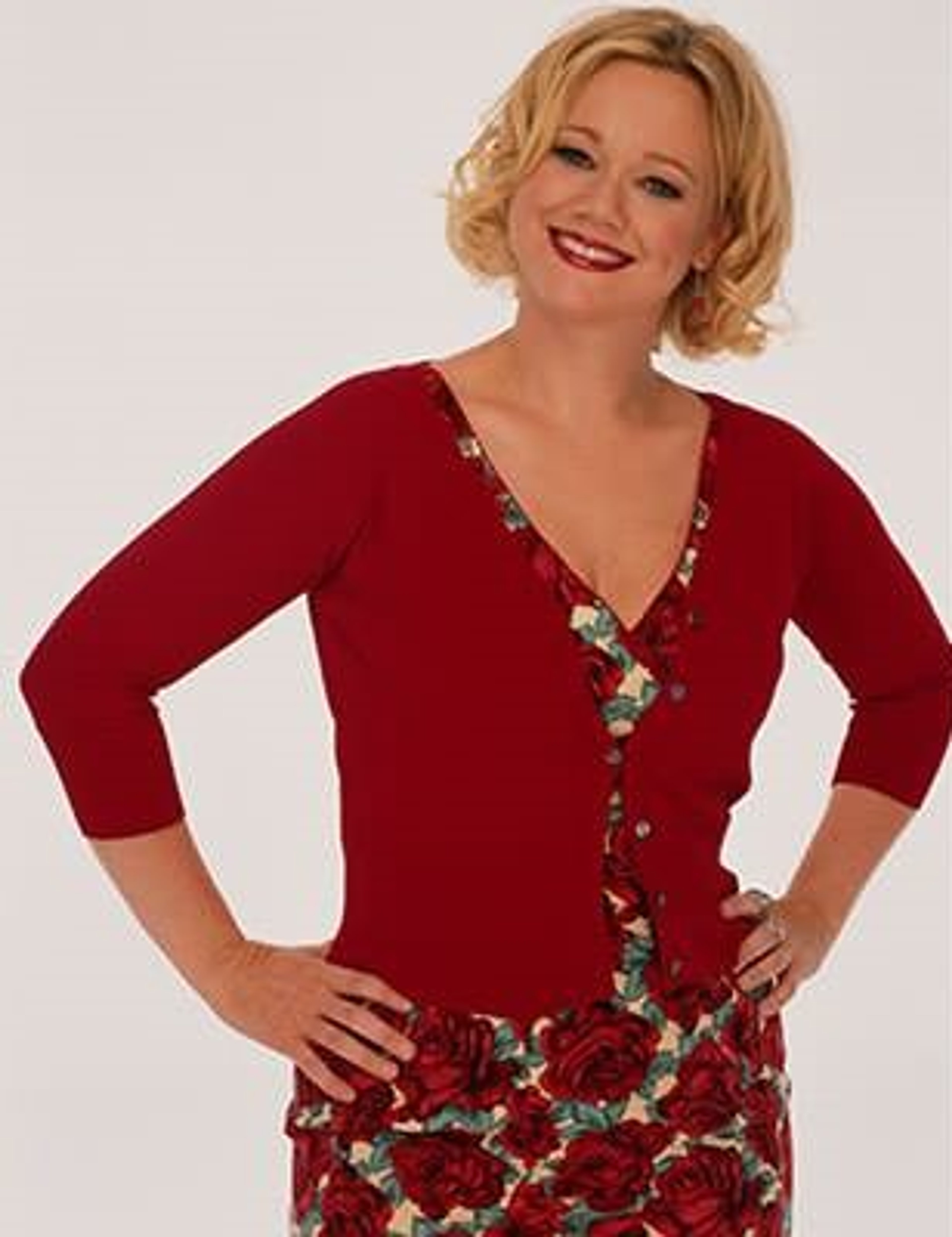 A smiling middle-aged woman with curly blonde hair wearing a red floral sweater