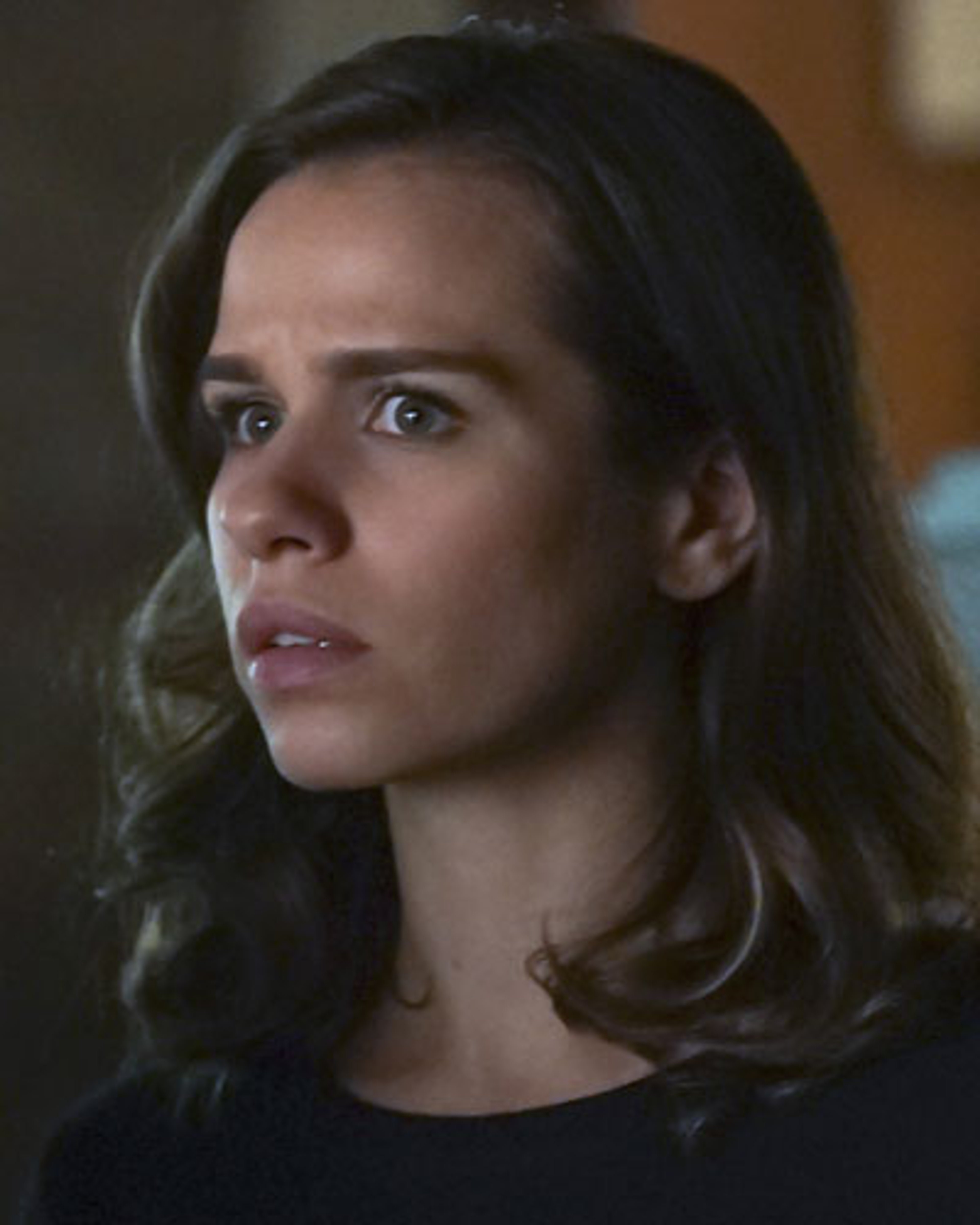 A young woman with dark hair and green eyes, wearing a dark shirt or jacket and looking serious.