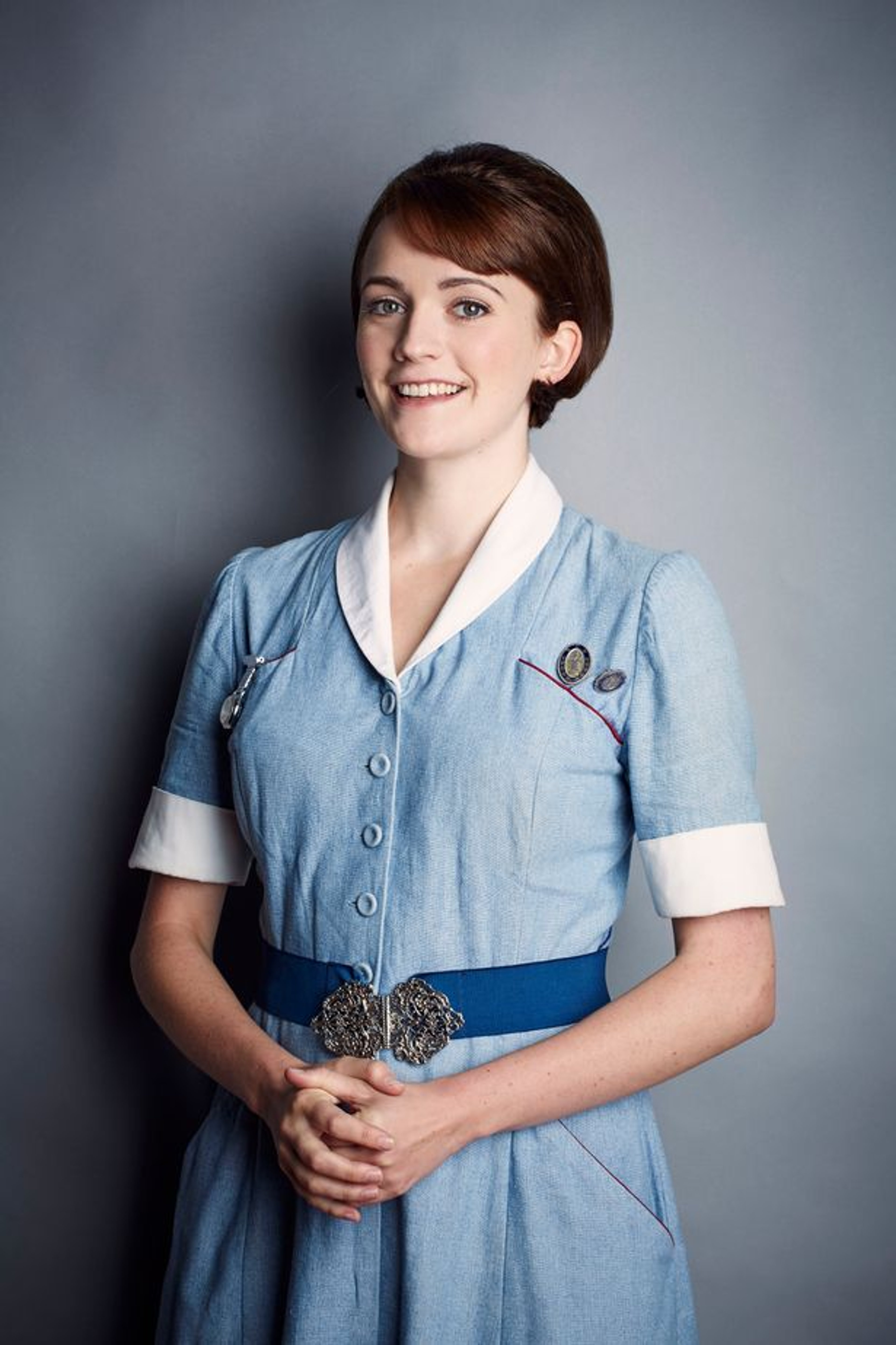 A young woman in a nurse's uniform smiling at the camera