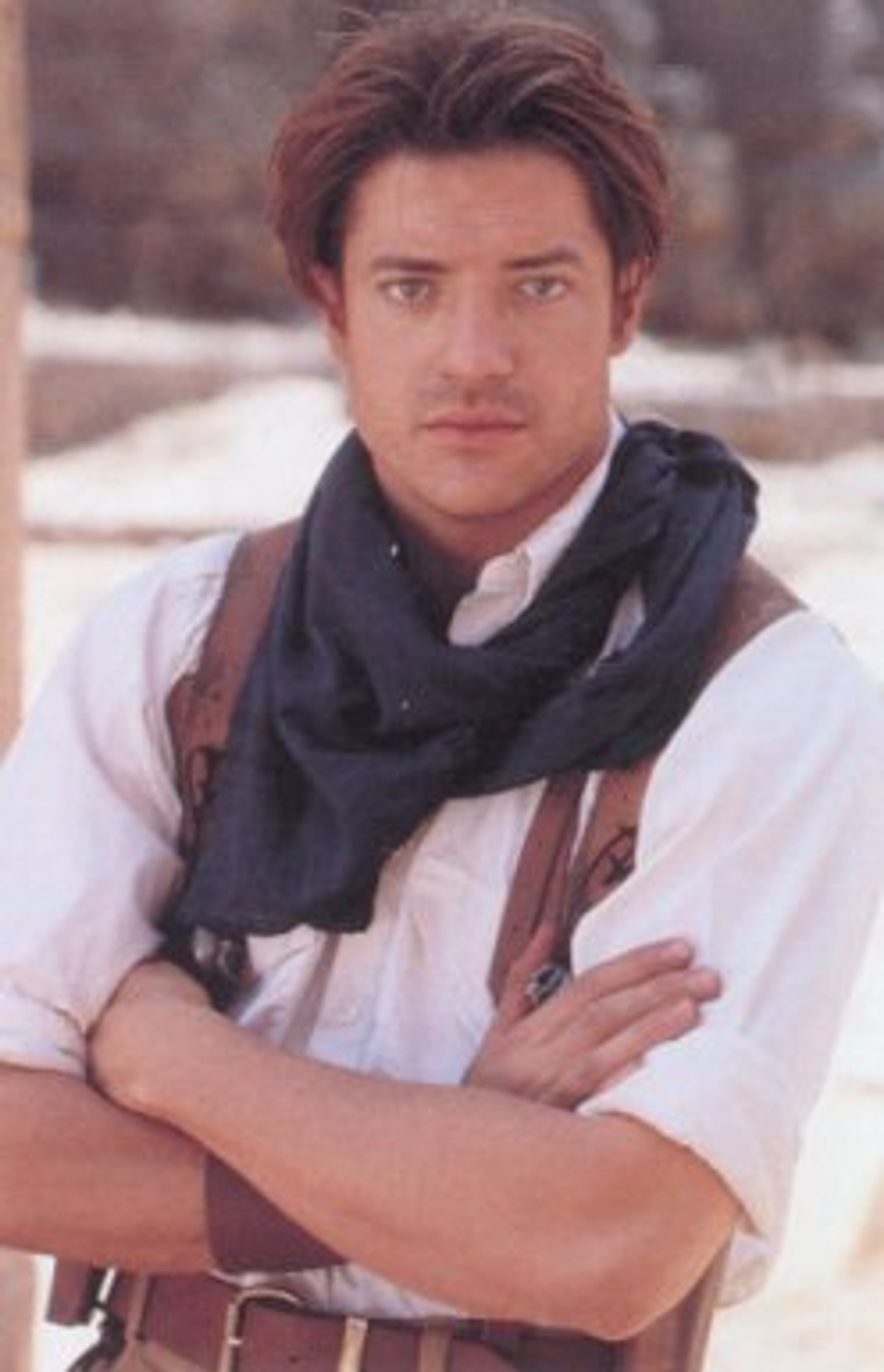 A man with short dark hair and a rugged appearance, wearing a white shirt and dark scarf.