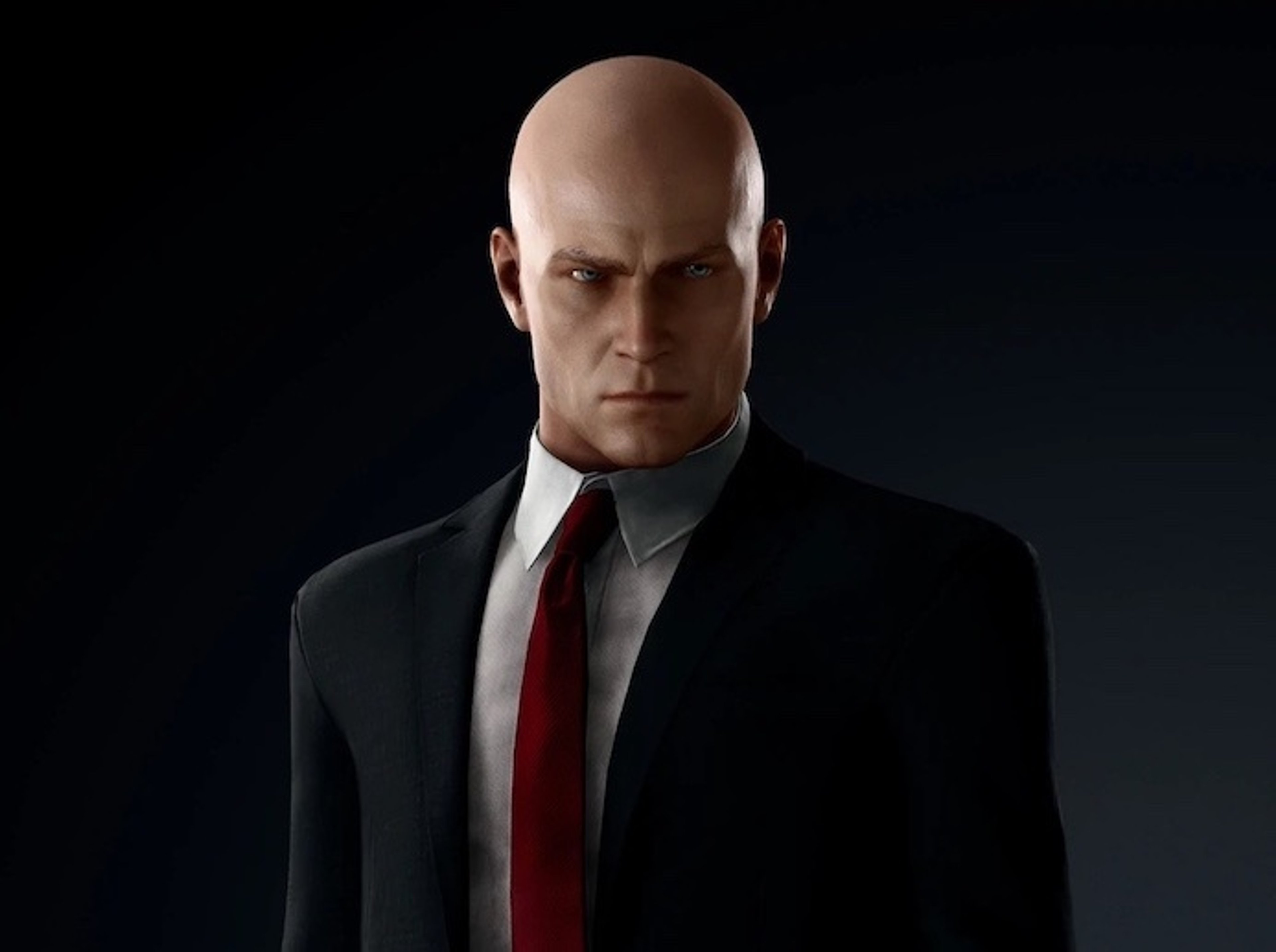 A bald, middle-aged man in a black suit and red tie, with a barcode tattoo on the back of his head.