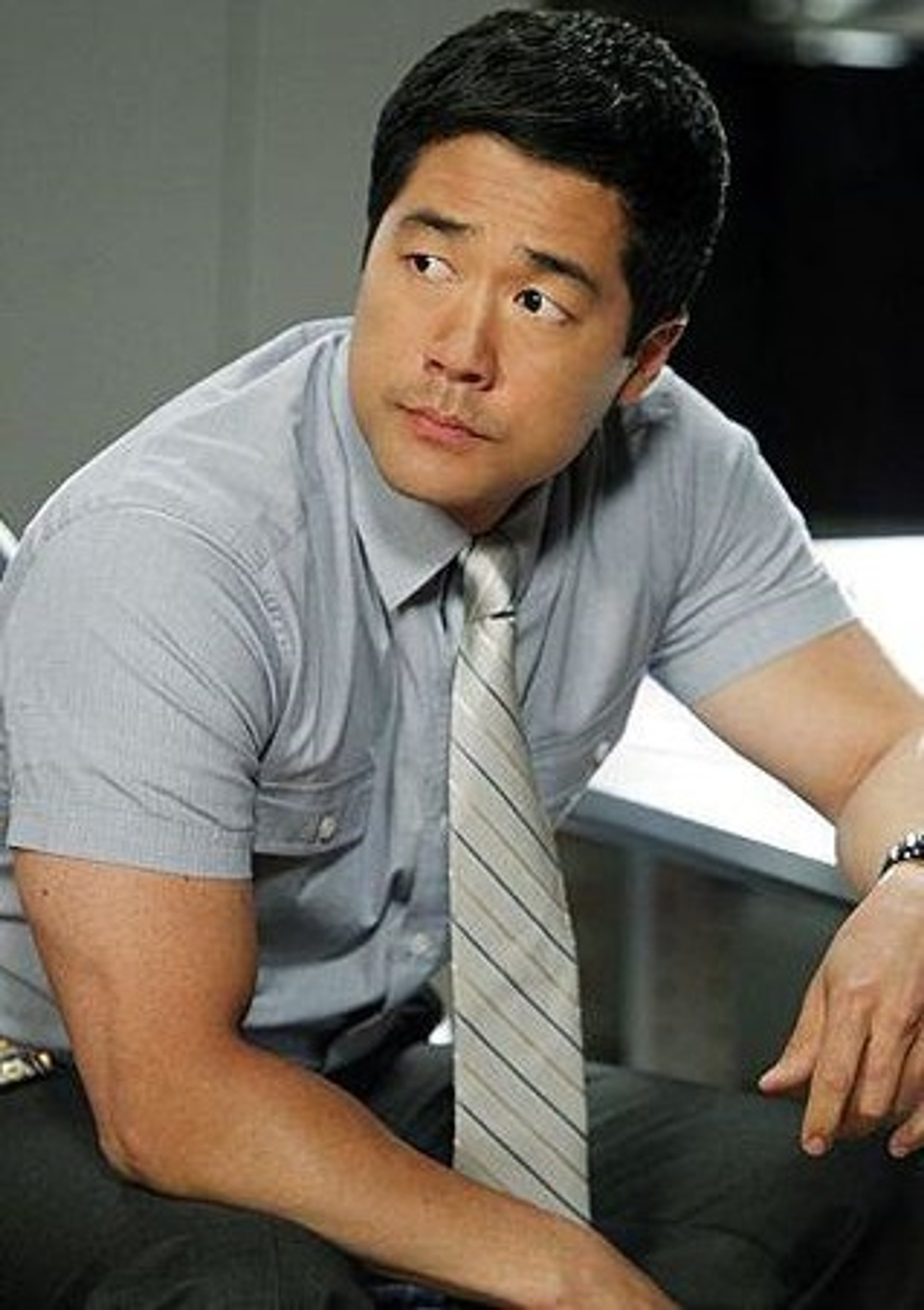 A middle-aged Asian man in a gray suit sitting at a desk