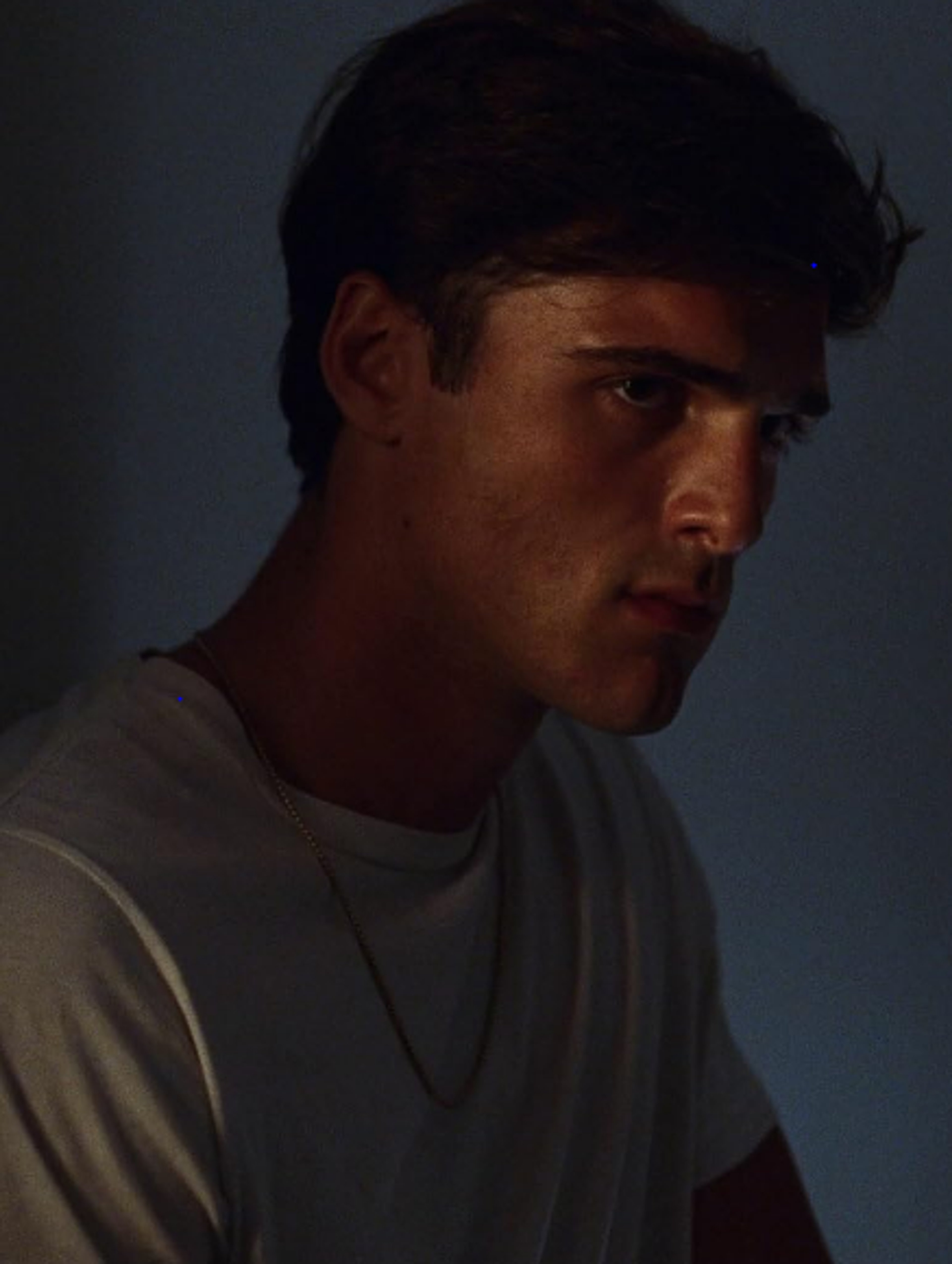 A close-up portrait of a young man with a serious, brooding expression