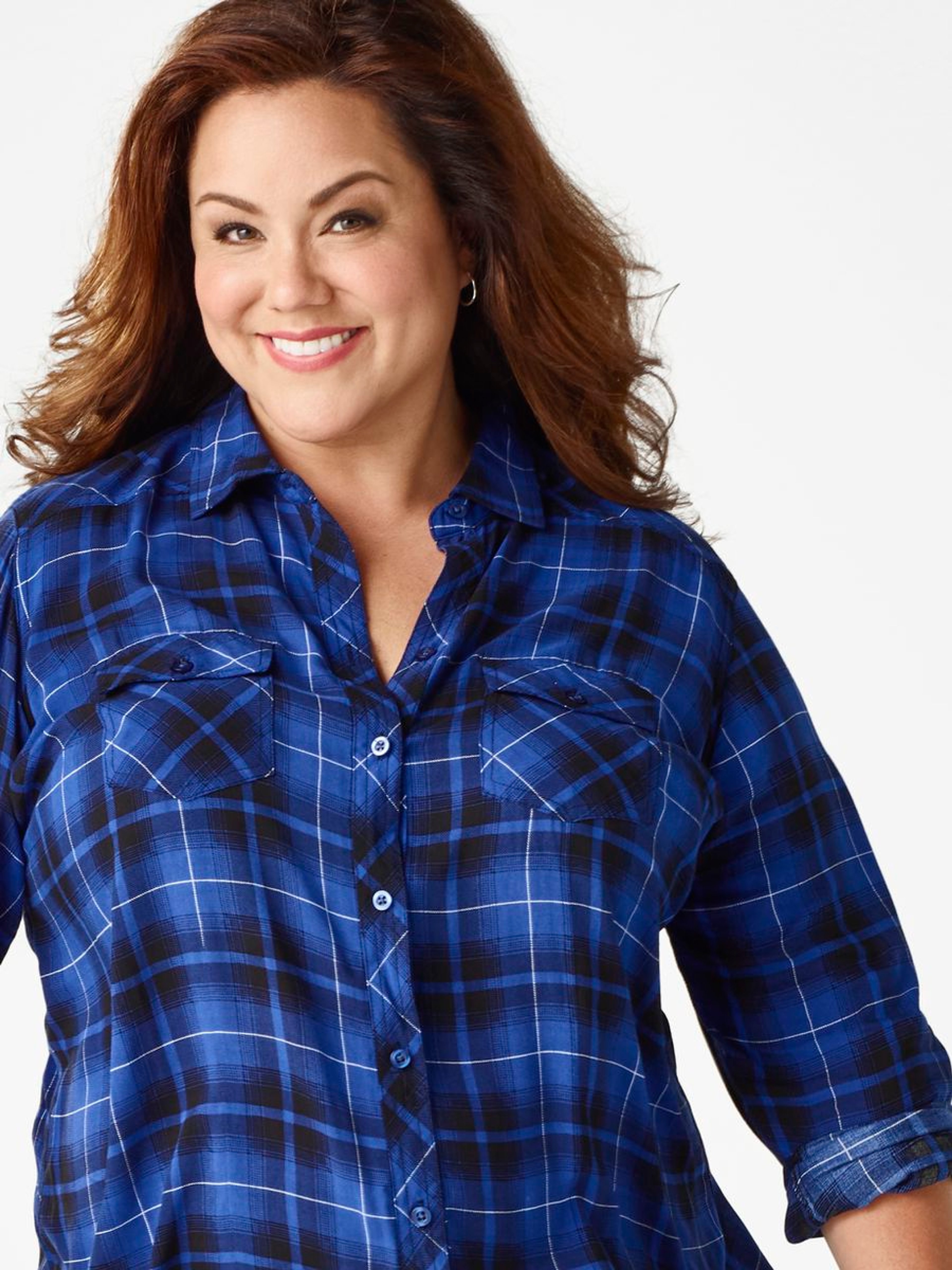 A middle-aged woman with curly brown hair wearing a blue and white plaid shirt