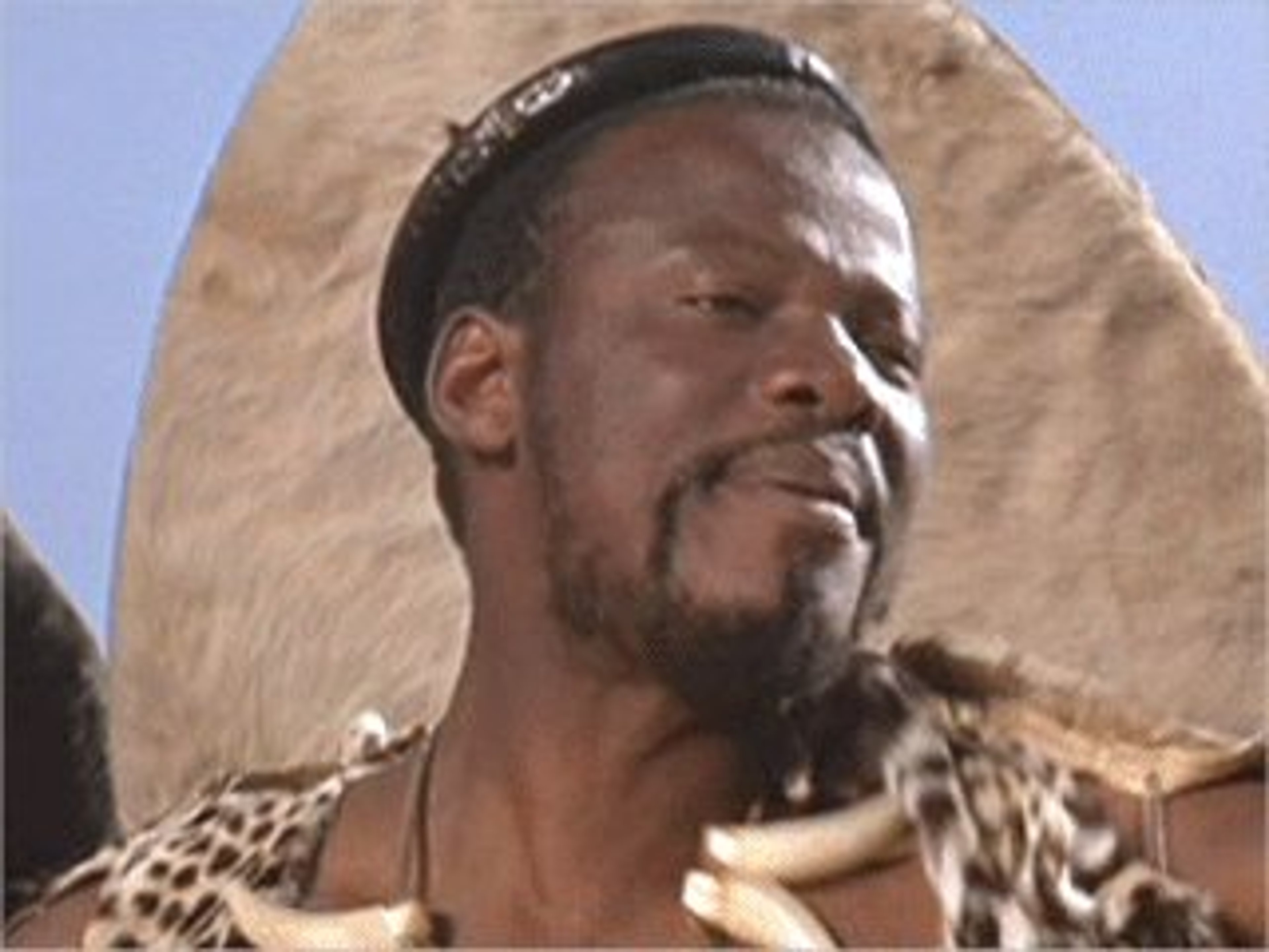 A middle-aged Black man in traditional Zulu attire with a serious expression