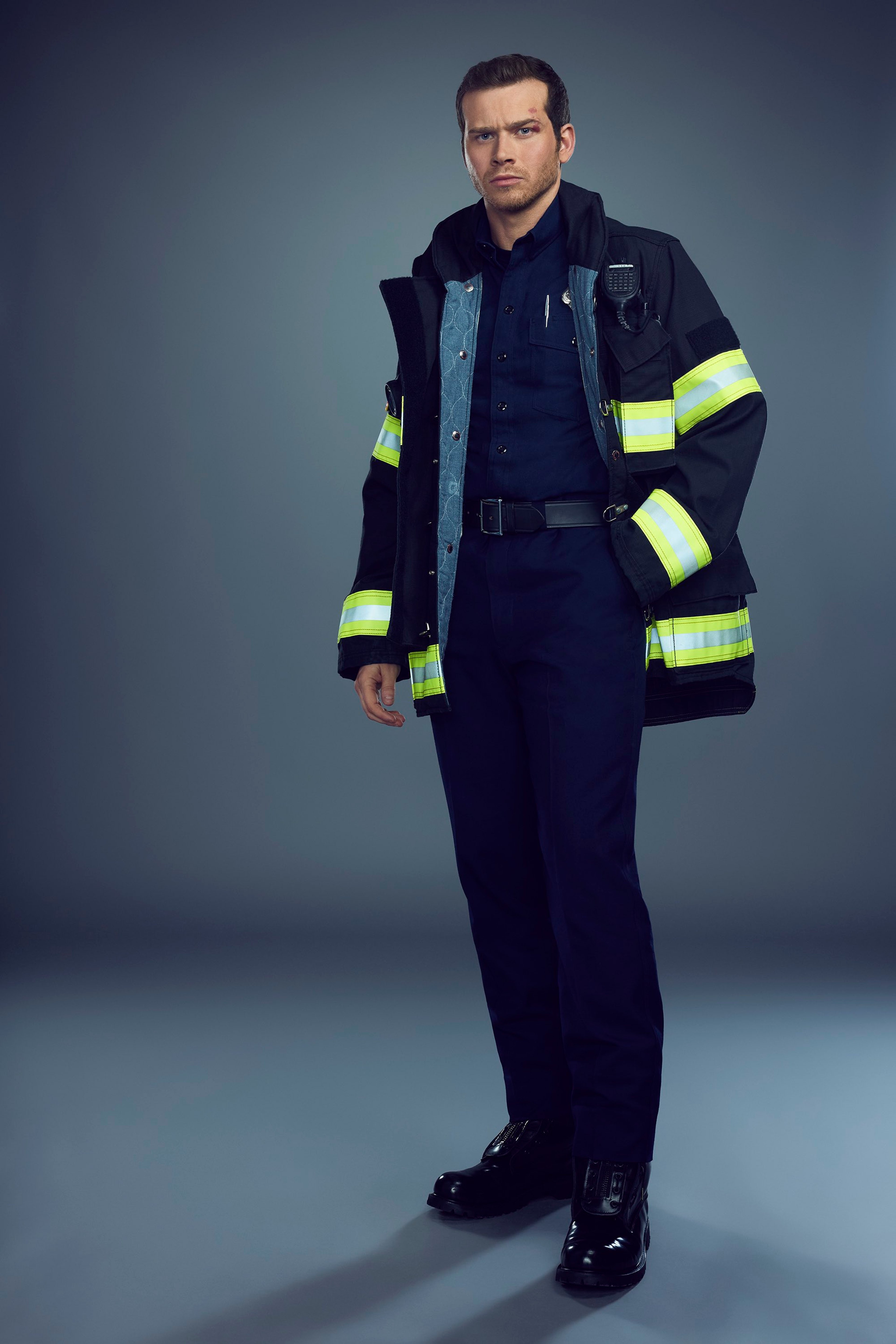 A firefighter in uniform standing in front of a gray background
