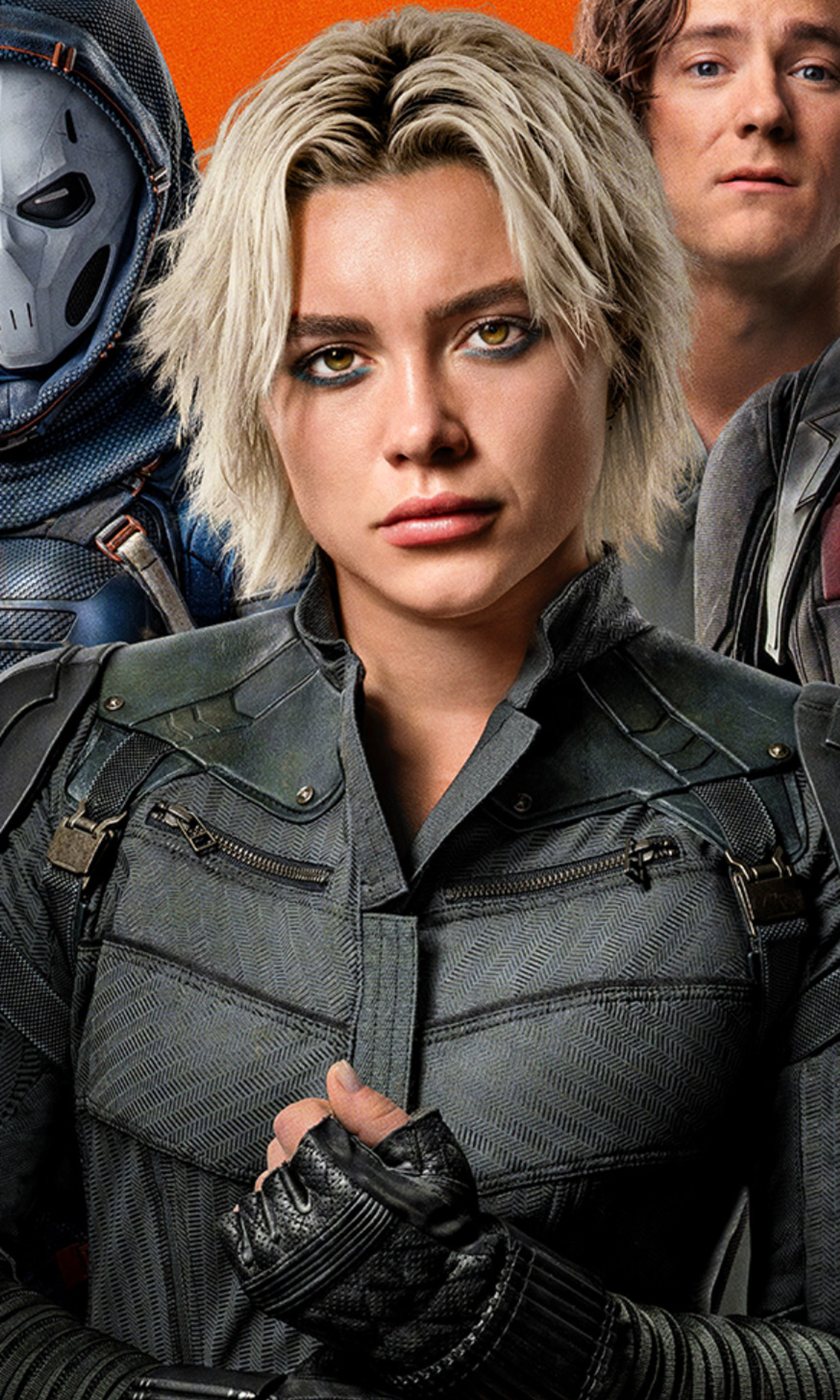 A woman with blonde hair wearing a tactical vest and gloves, with a serious expression on her face.