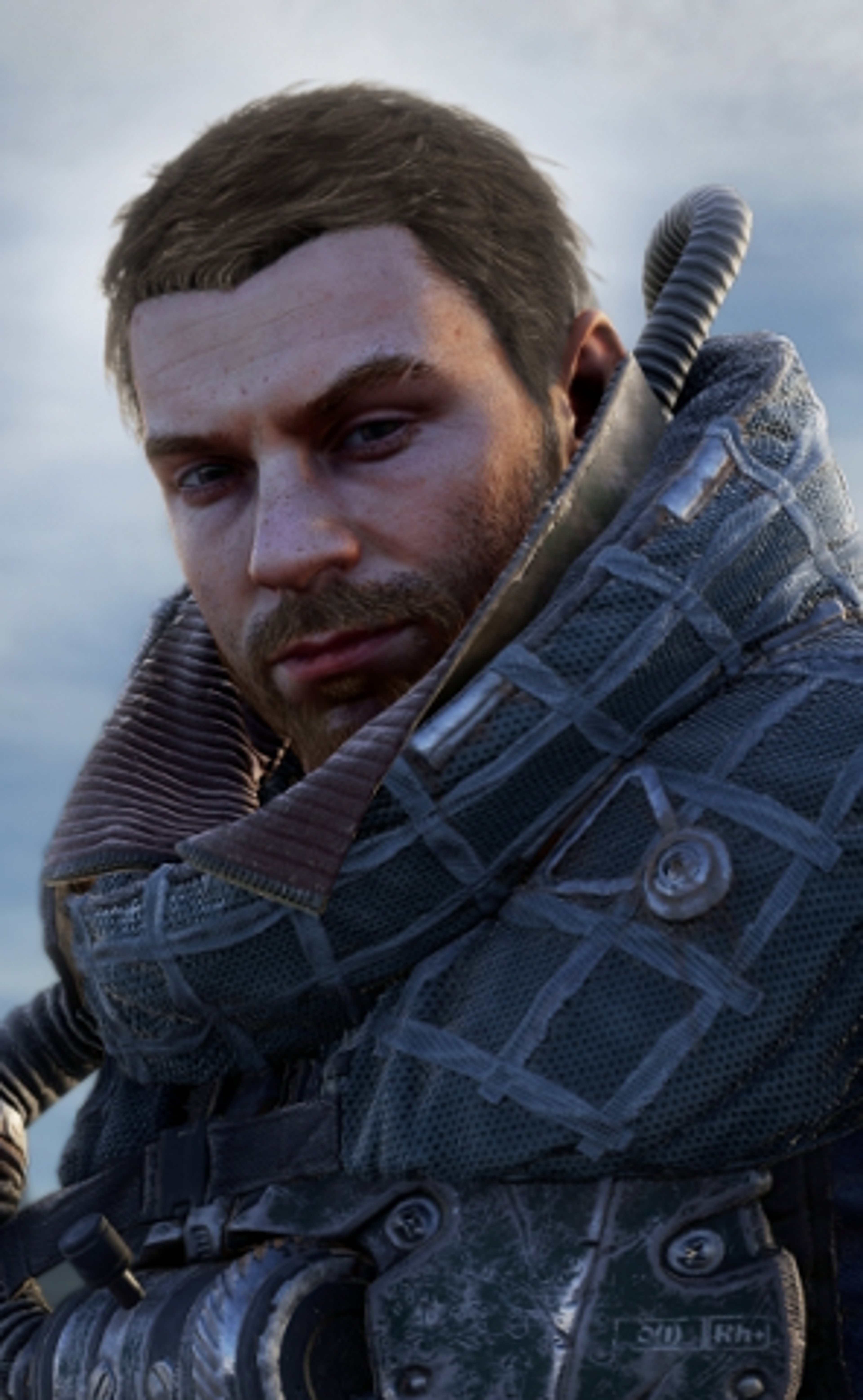 A young man with brown hair and eyes wearing a dark military jacket, looking serious and determined.