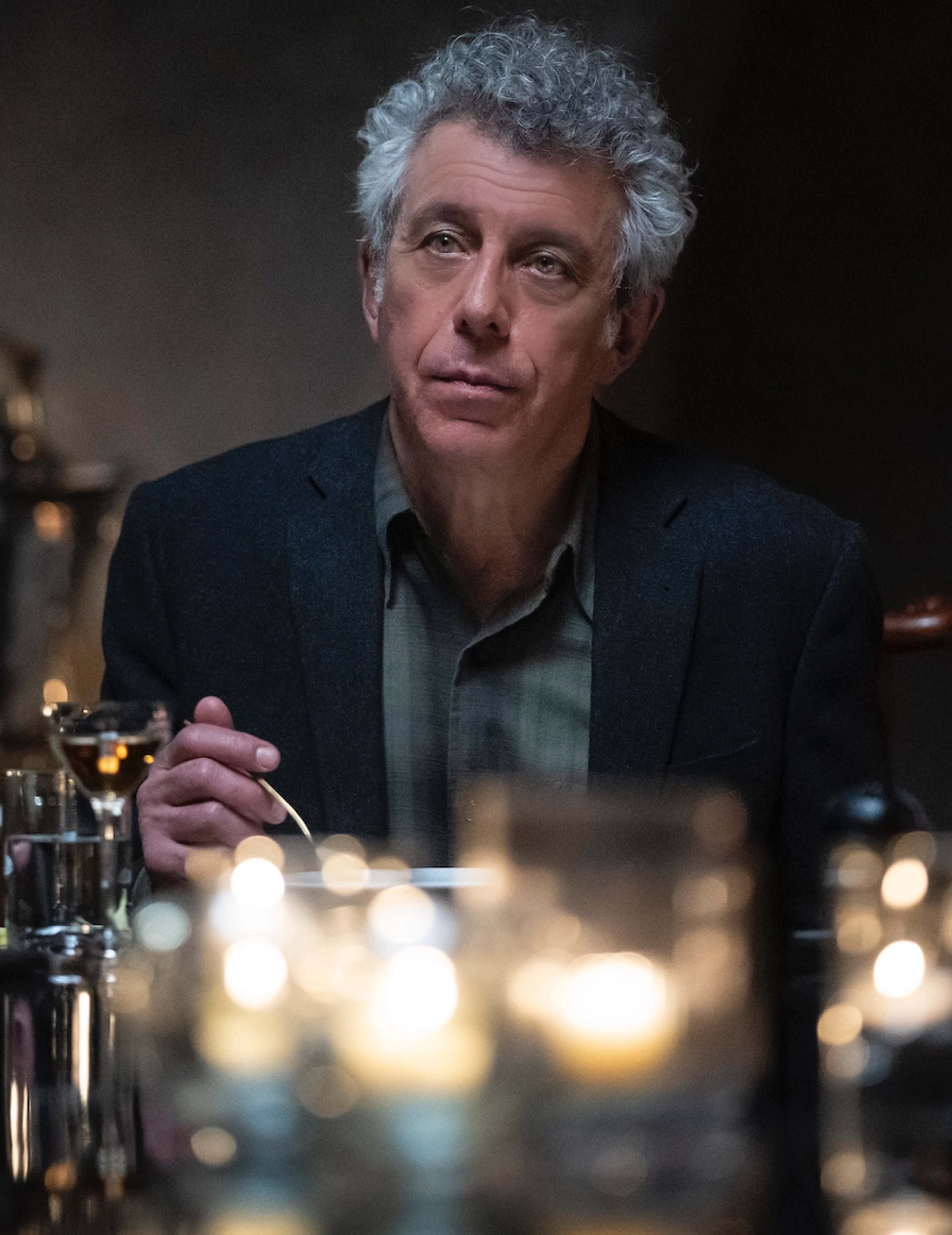 An older man with gray hair sitting at a table, looking pensive.