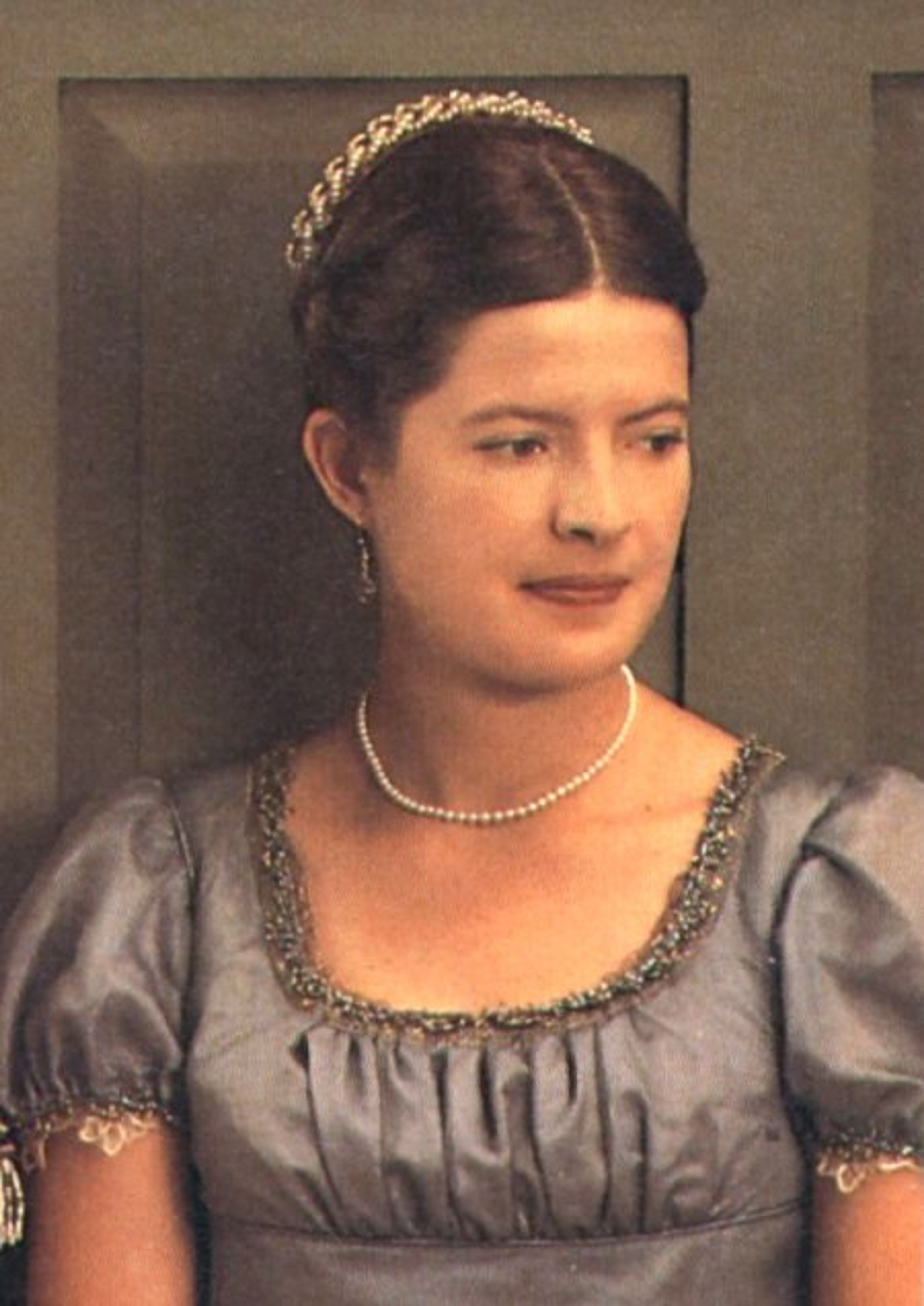 A woman in a gray dress with an updo hairstyle and pearl necklace, in a formal portrait setting.