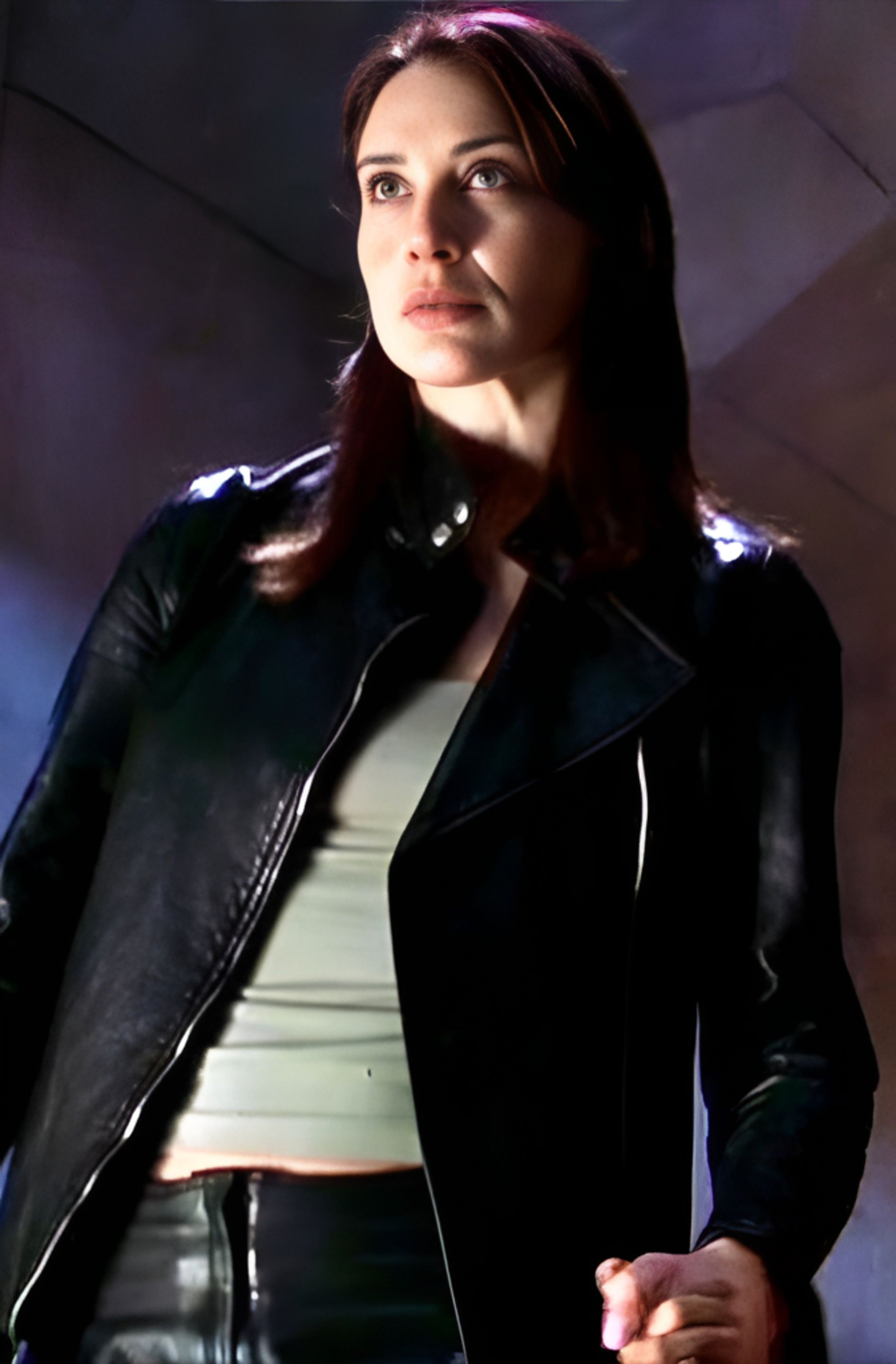A woman with dark hair wearing a black leather jacket in a dimly lit setting