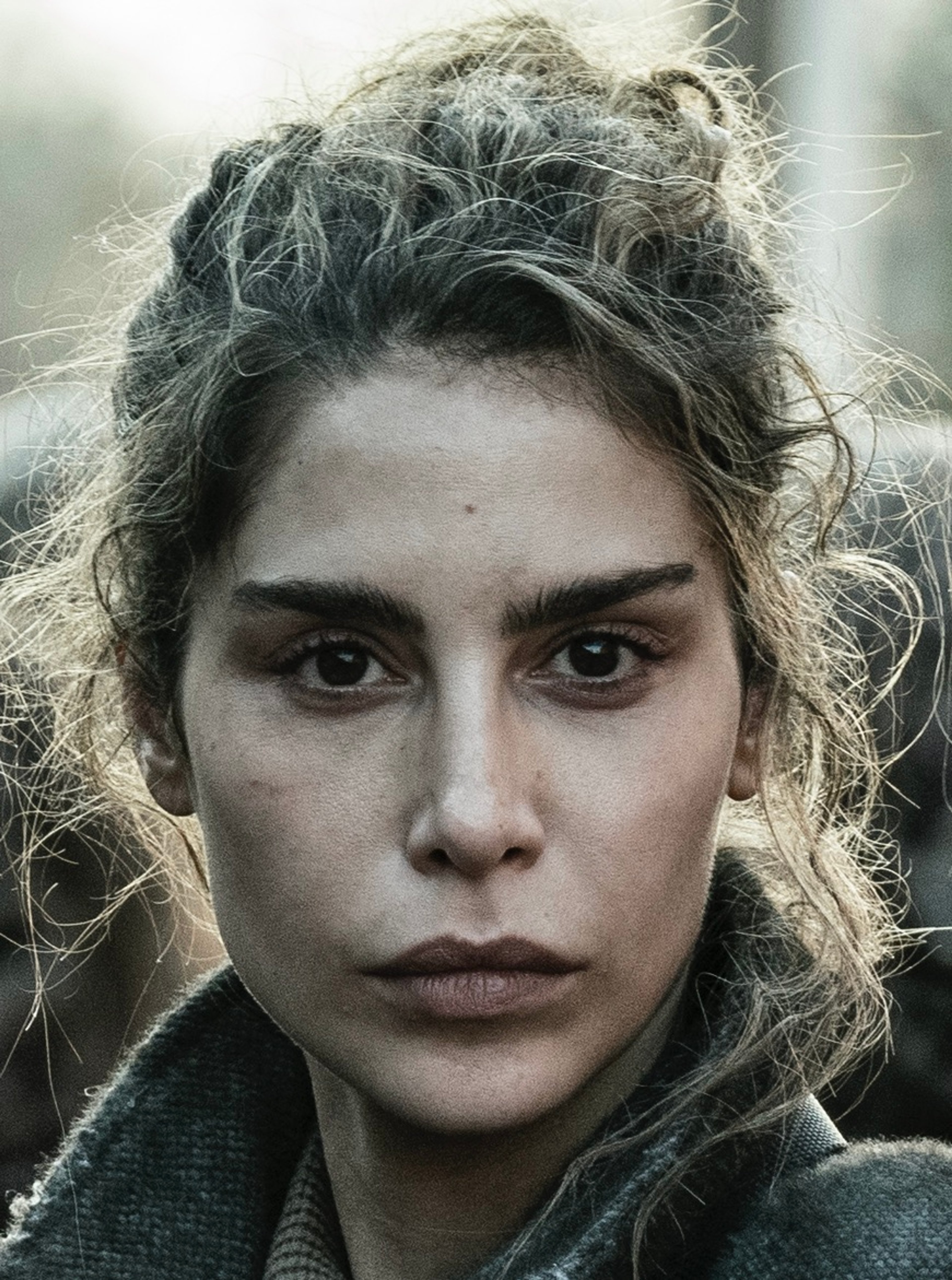 A woman with curly hair and a serious expression, wearing a dark jacket or coat