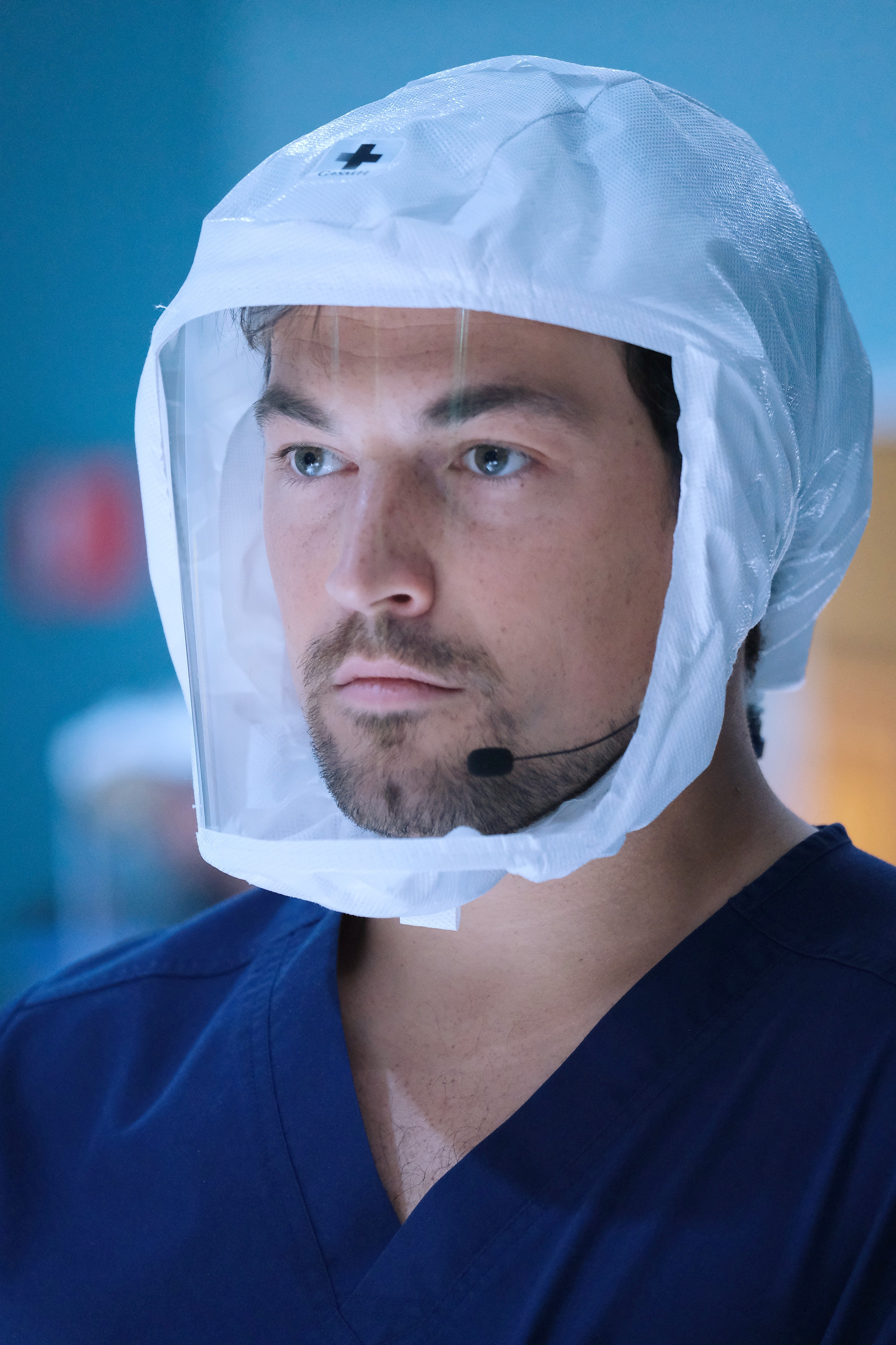A man in a white protective suit and mask, likely a medical professional, with a serious expression on his face.