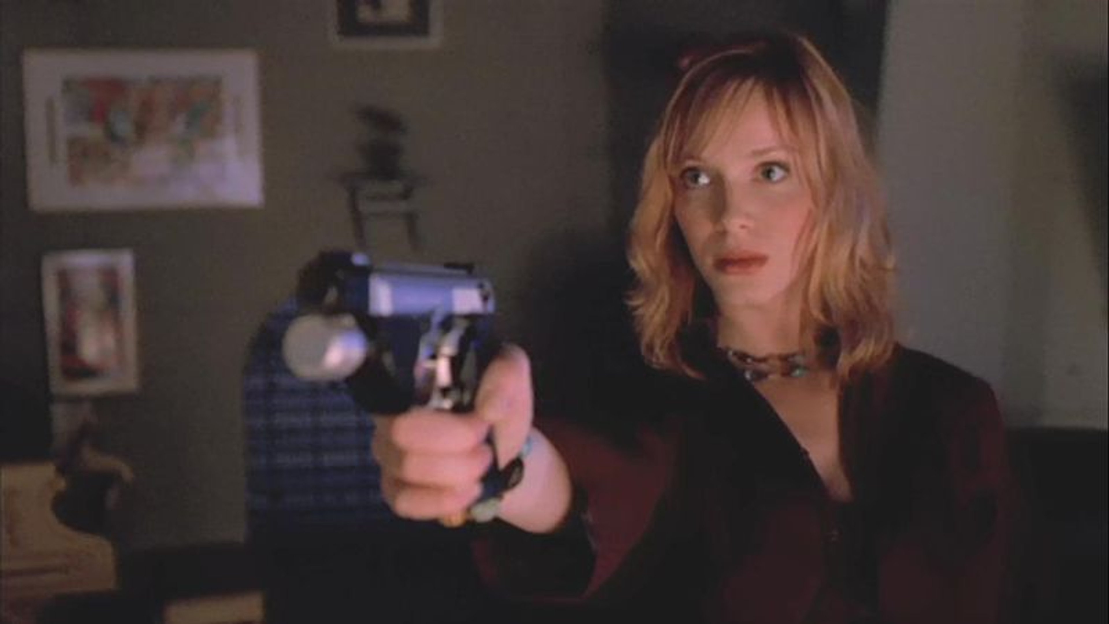 A woman with blonde hair holding a gun in a dimly lit room