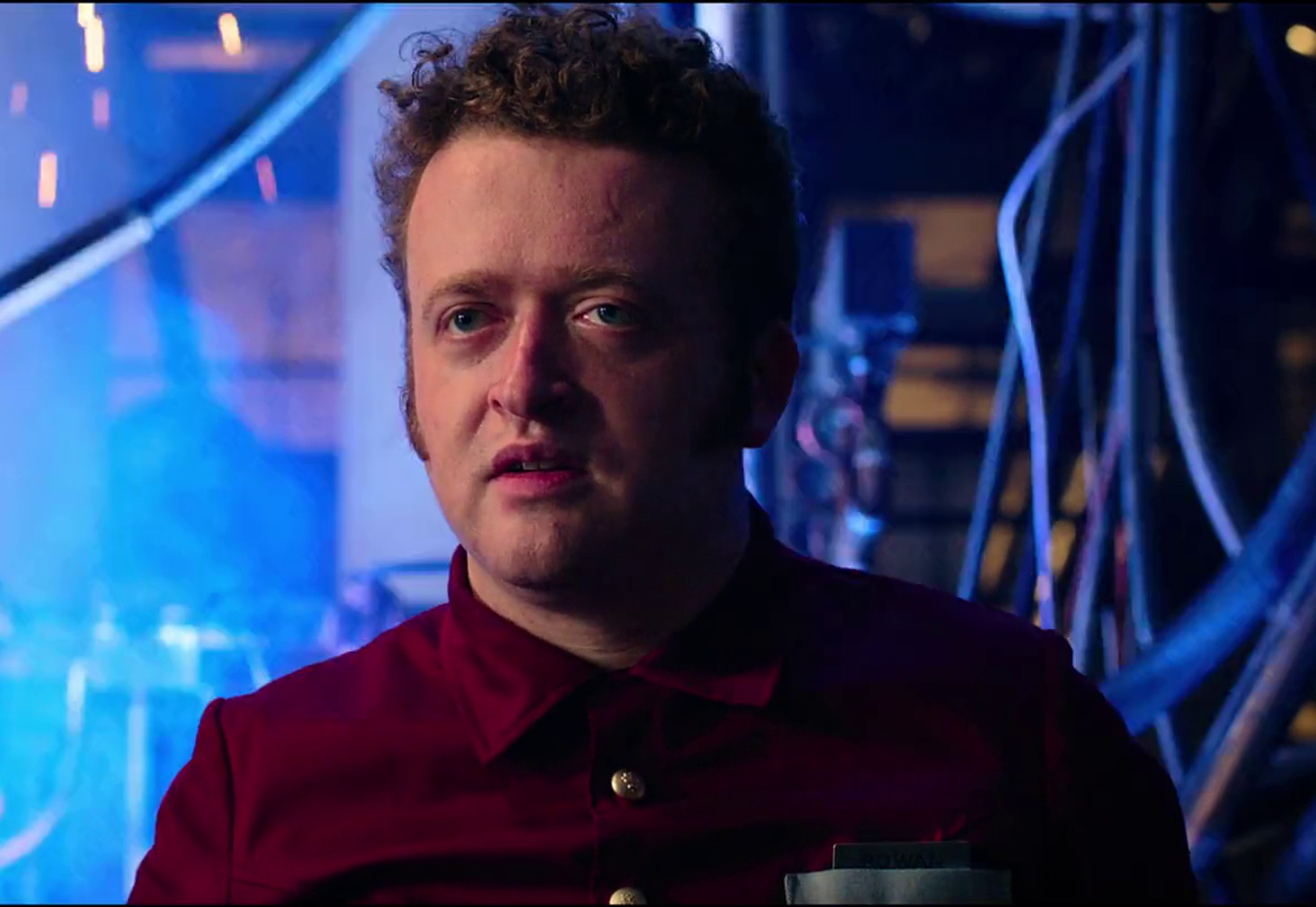 A middle-aged man with curly brown hair in a red shirt standing in a technological setting