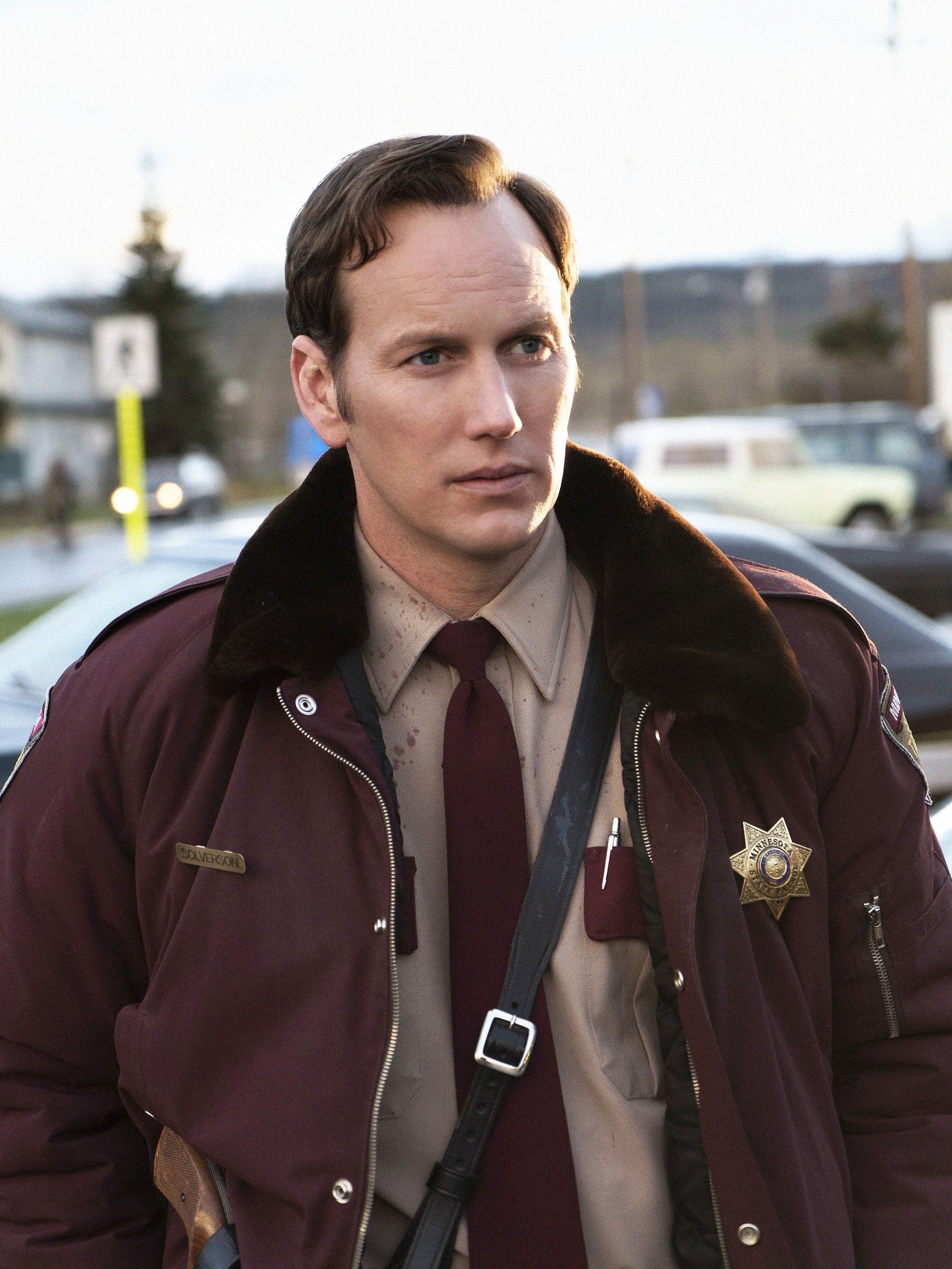 A middle-aged man in a burgundy law enforcement uniform standing outdoors