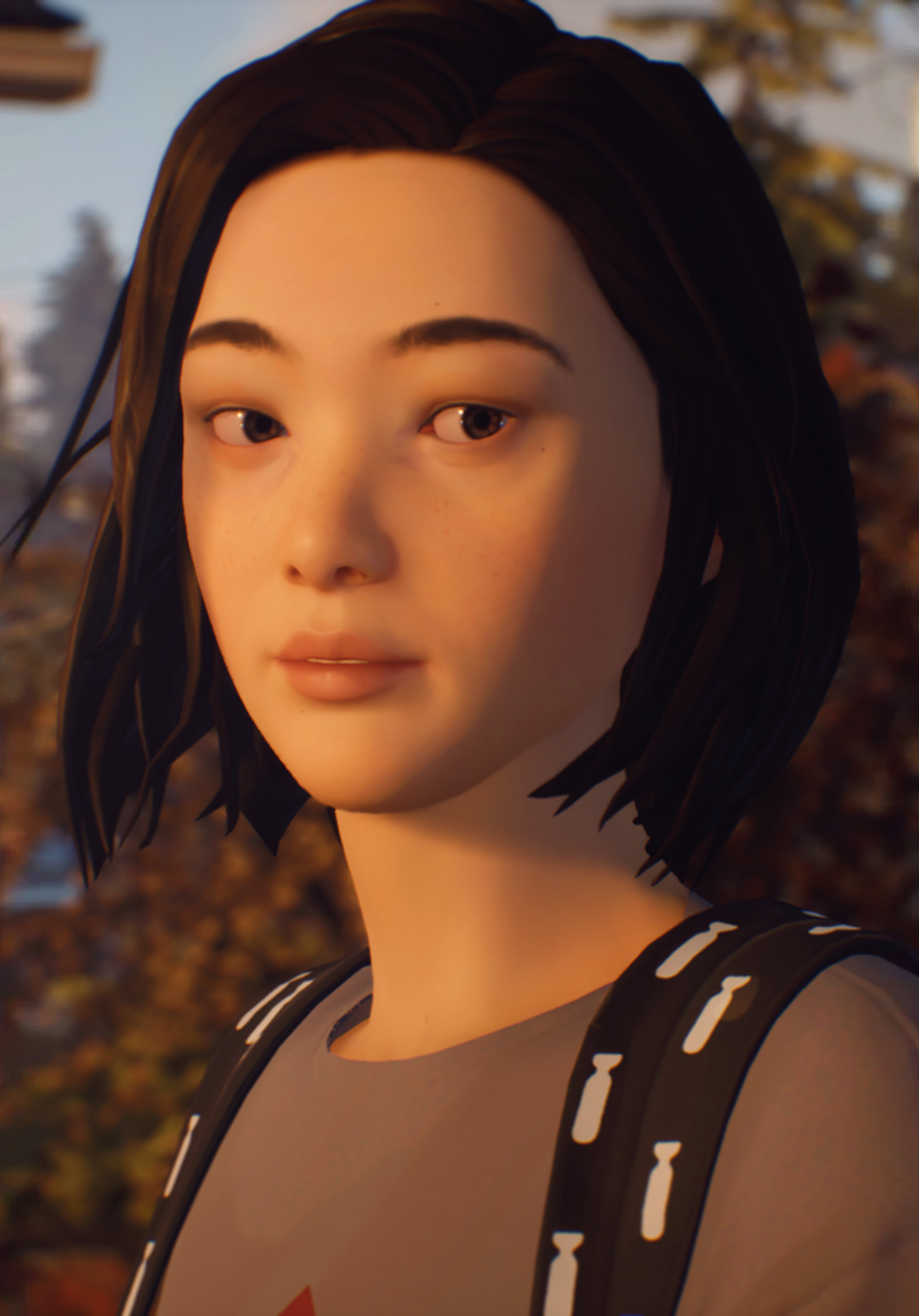 A young woman with dark hair and a serious expression, wearing a striped shirt and standing outdoors.