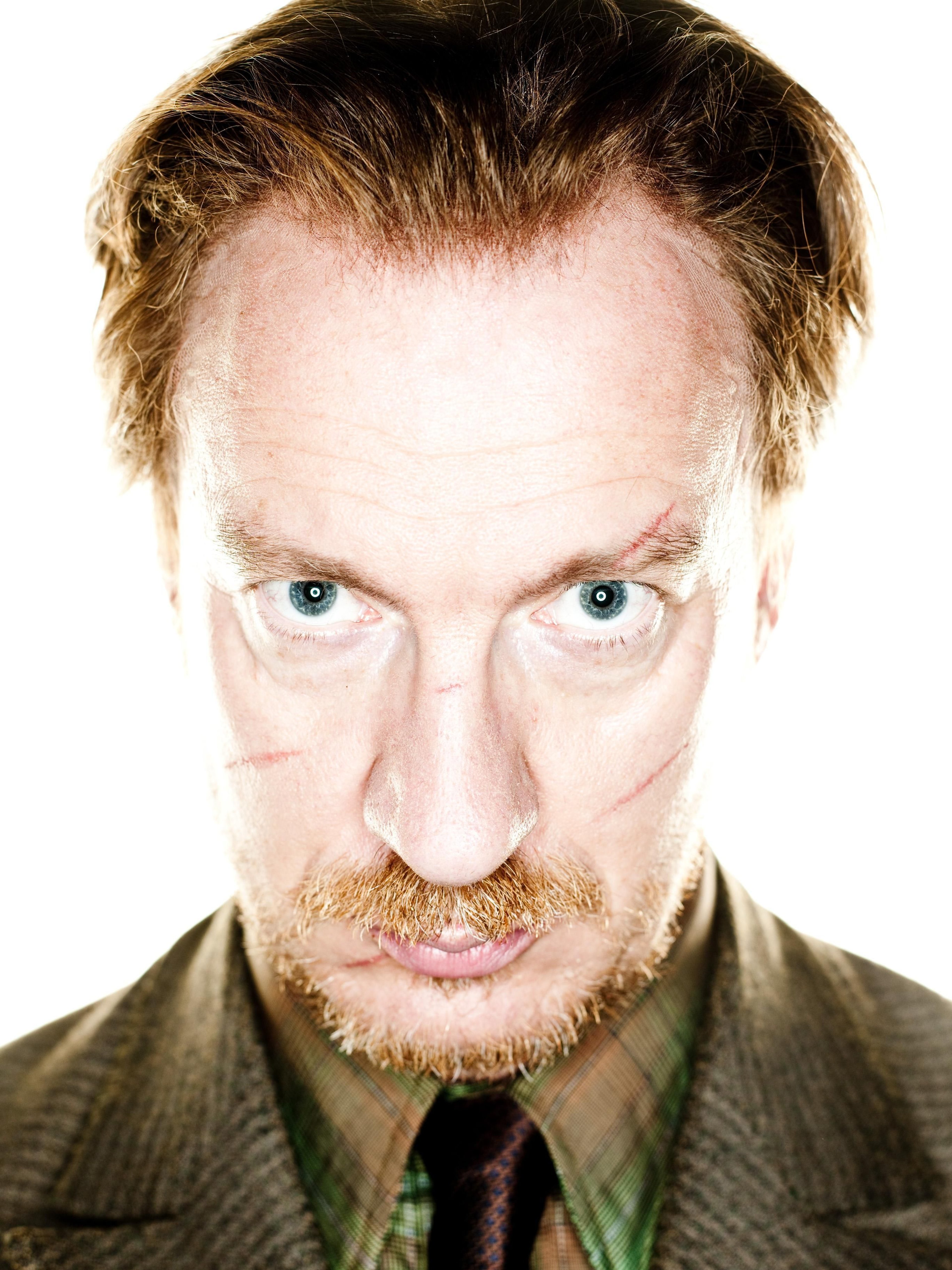 A middle-aged man with graying hair and a beard, wearing a brown jacket and looking serious.