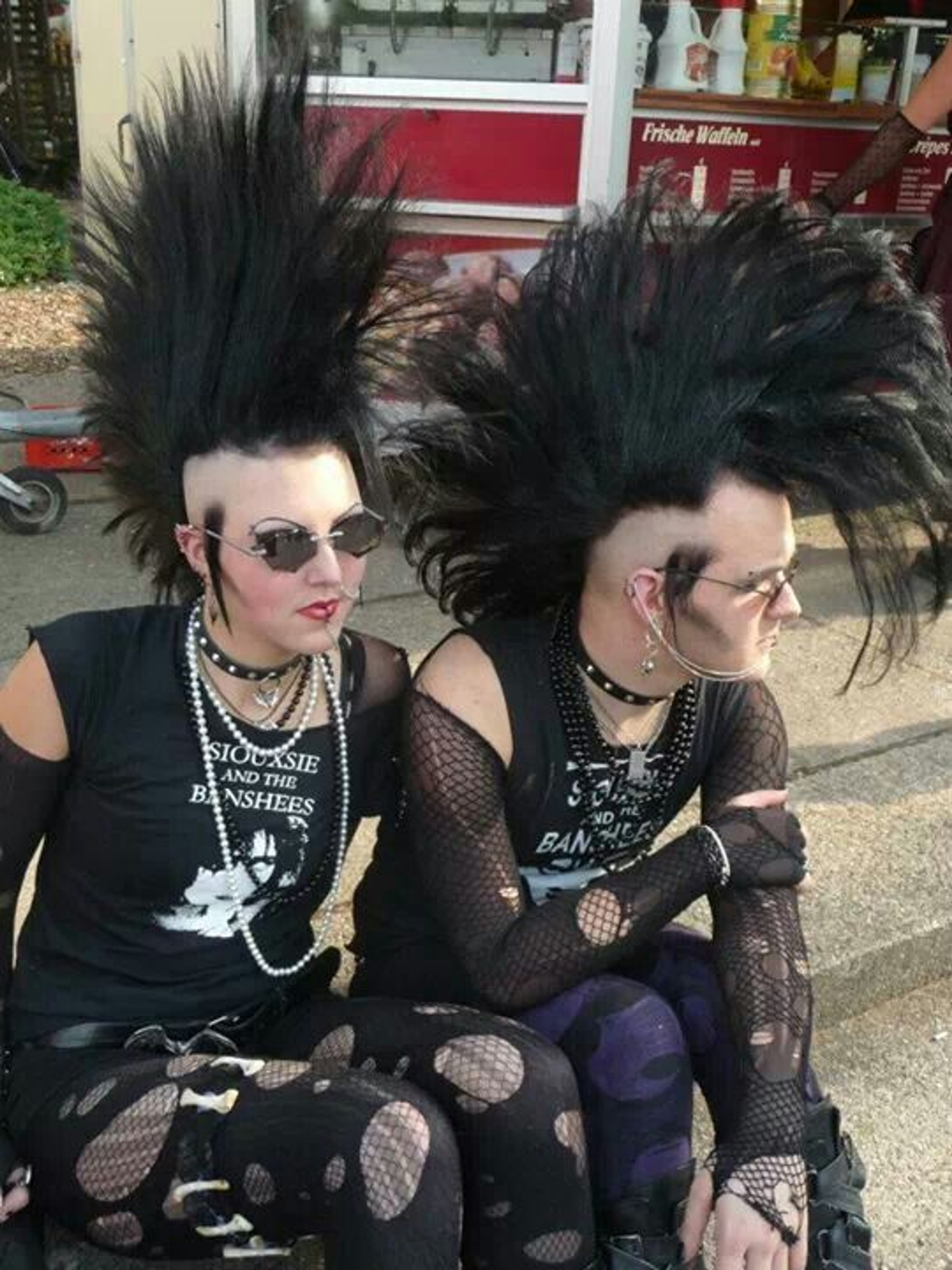 Two individuals with punk rock-inspired appearances sitting on a bench or ledge outdoors