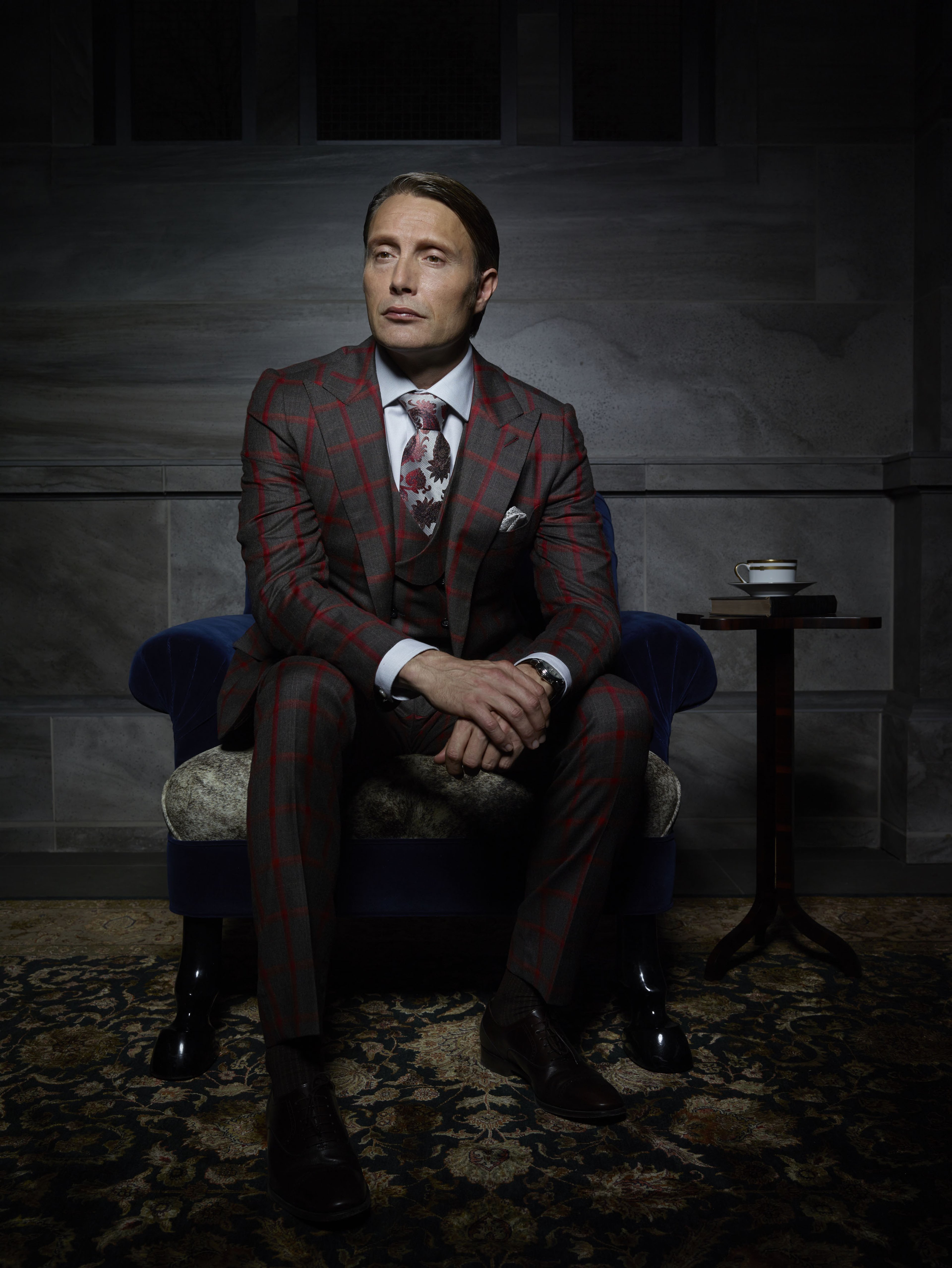 A well-dressed man in a red suit jacket sitting in a chair