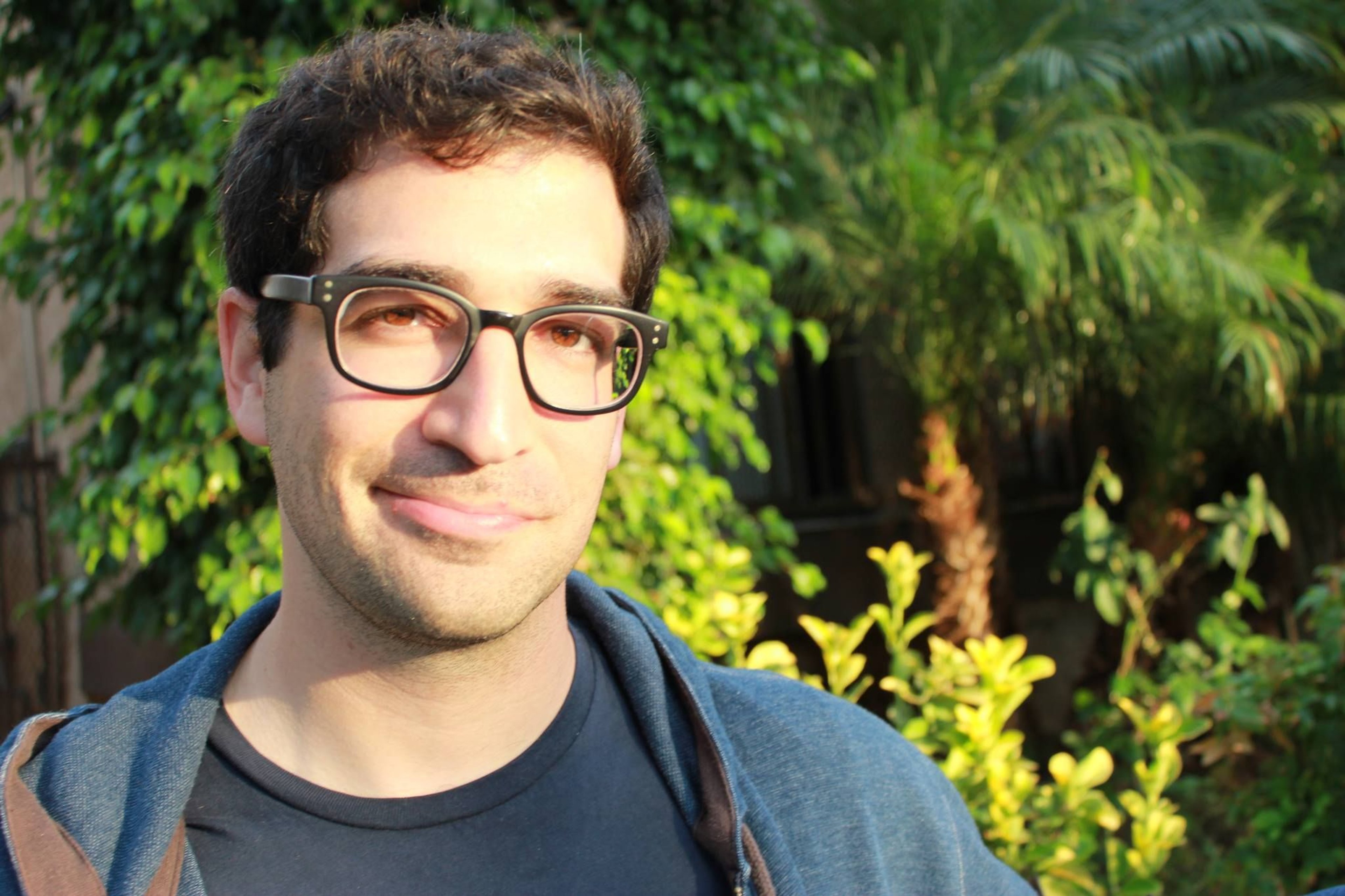 A middle-aged man with glasses and short dark hair in a blue shirt, standing in an outdoor setting.