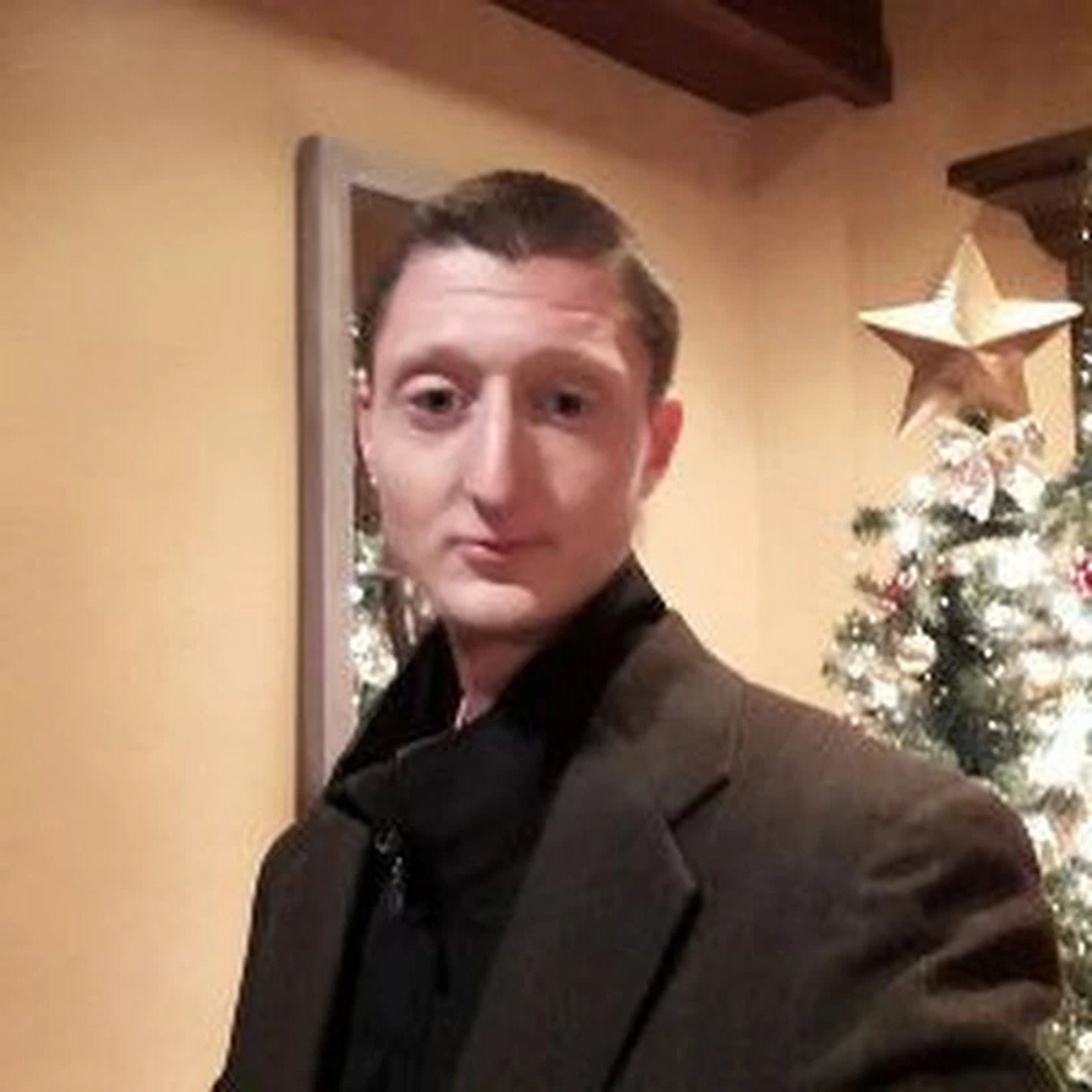 A middle-aged man with a beard standing in front of a Christmas tree