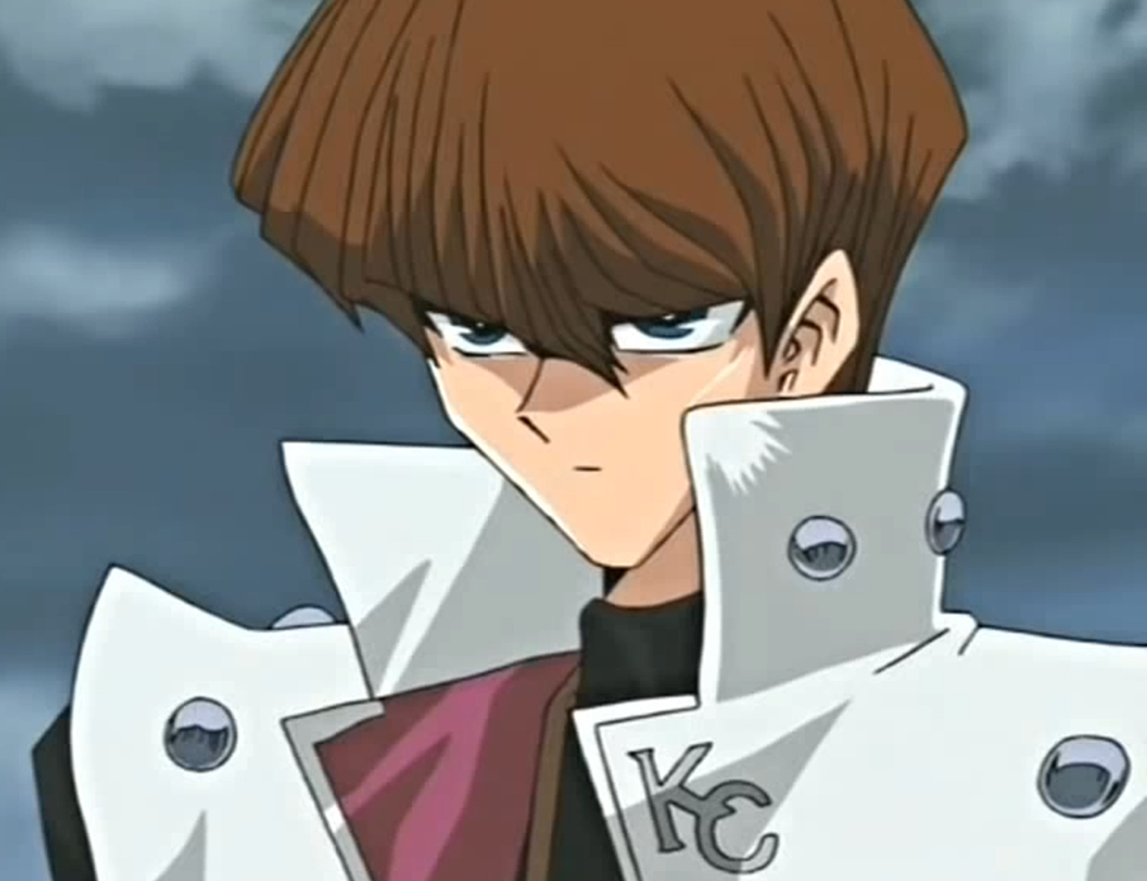 A young man with brown hair and blue eyes wearing a white coat with buckles and straps, holding a technological device.