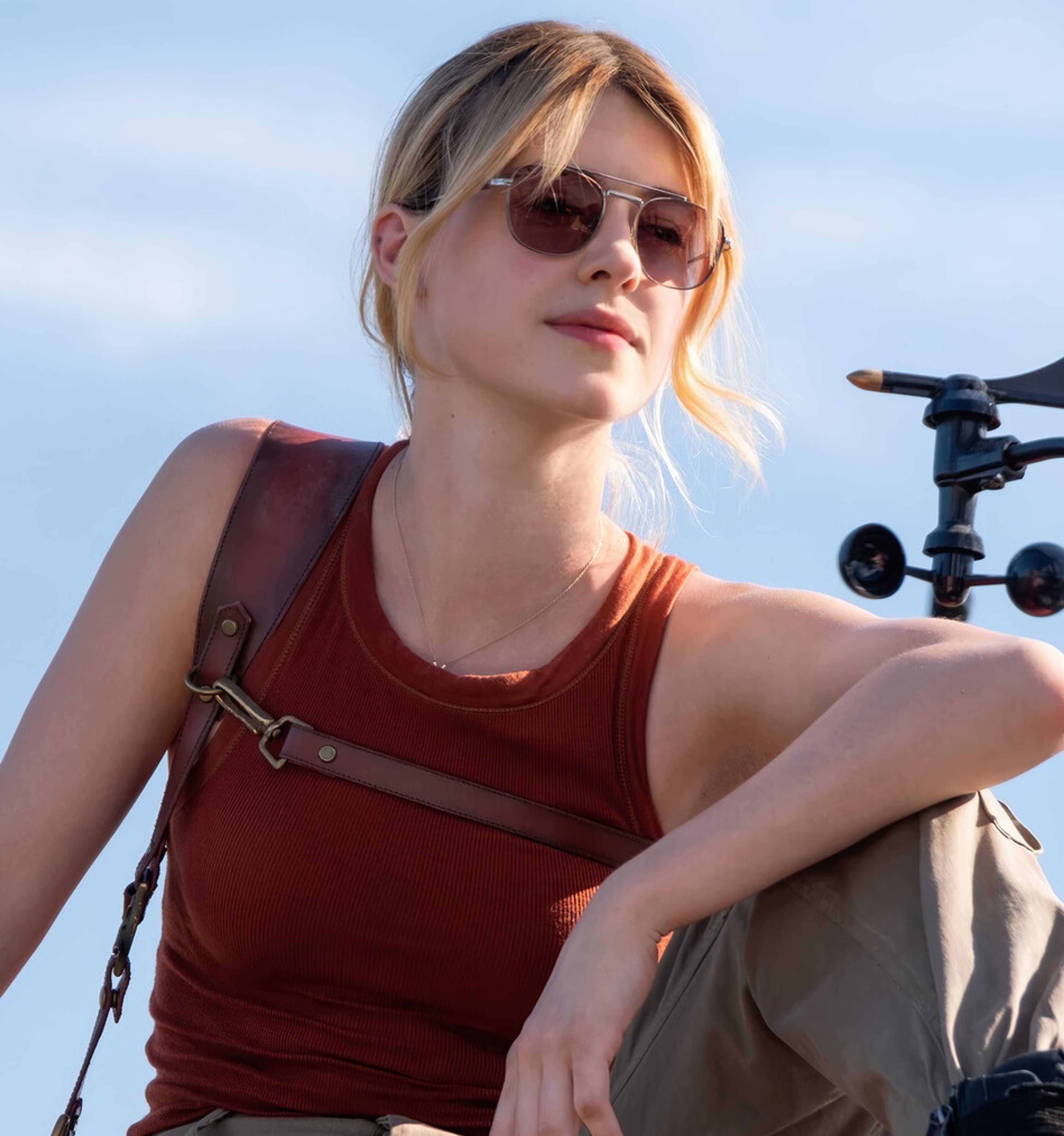 A young woman with blonde hair wearing a red tank top and sunglasses, standing outdoors.