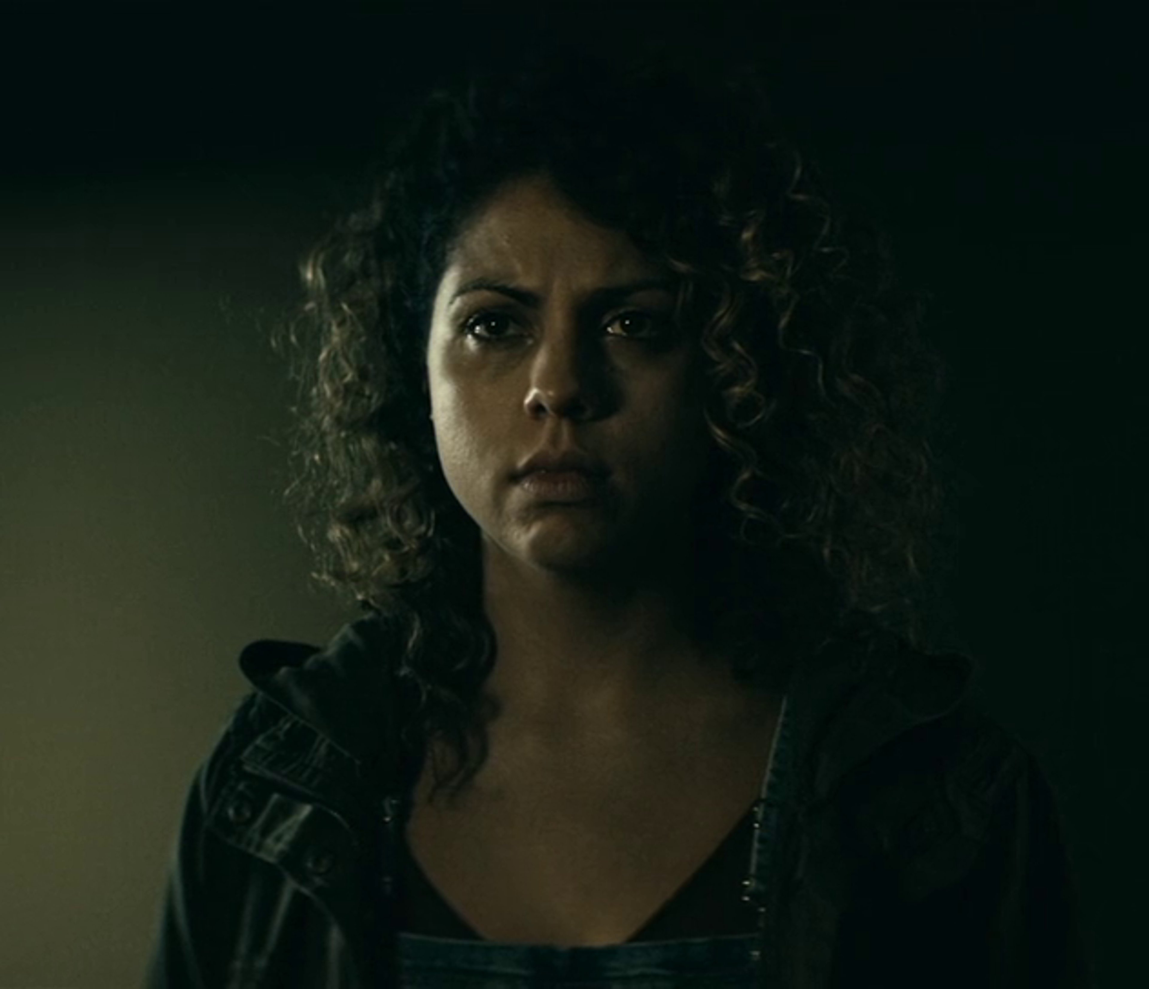 A young woman with curly brown hair and a serious expression