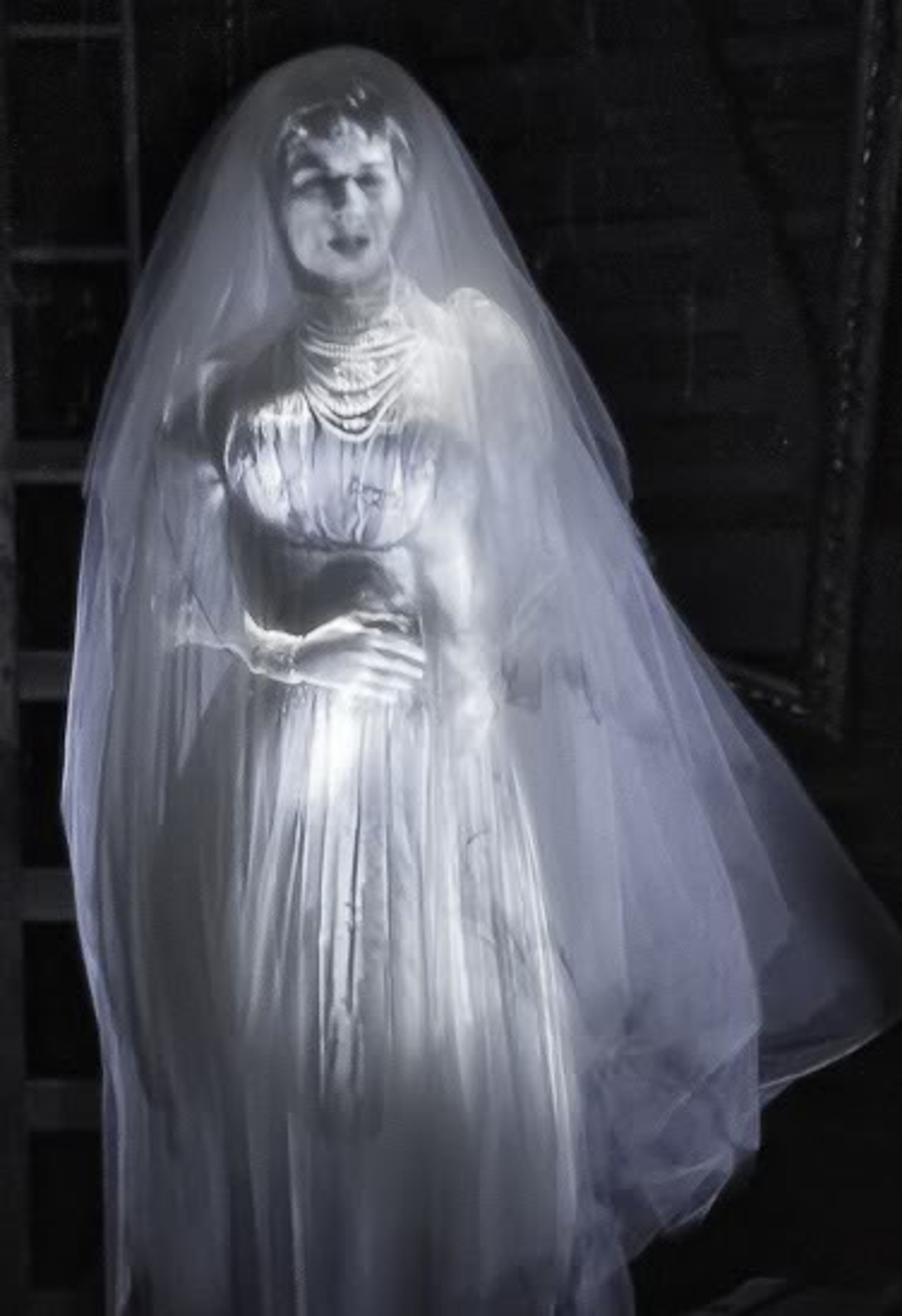 A woman in a long, white wedding dress standing in a dimly lit, gothic-style setting