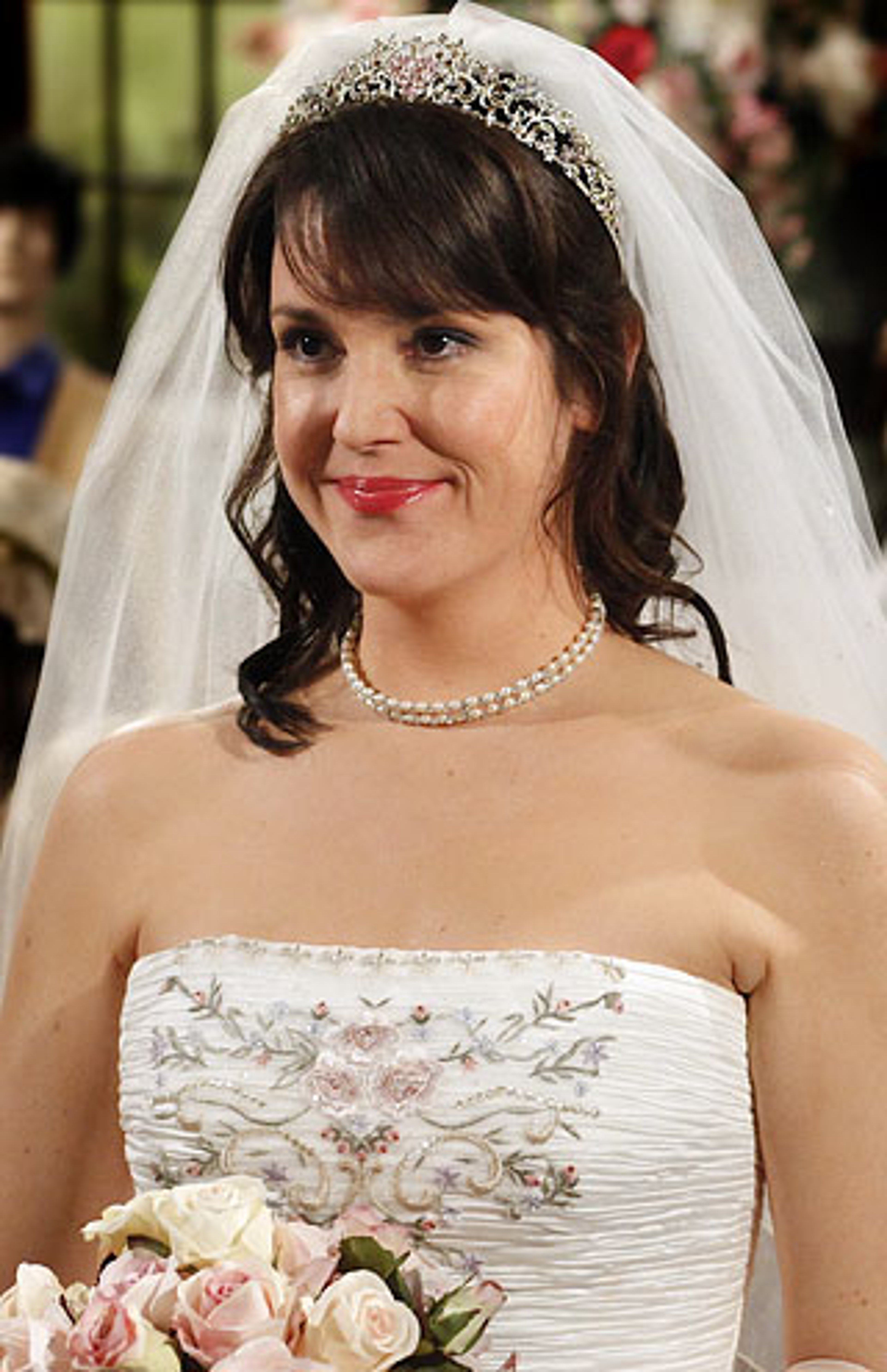 A woman in a white wedding dress and veil, smiling at the camera.