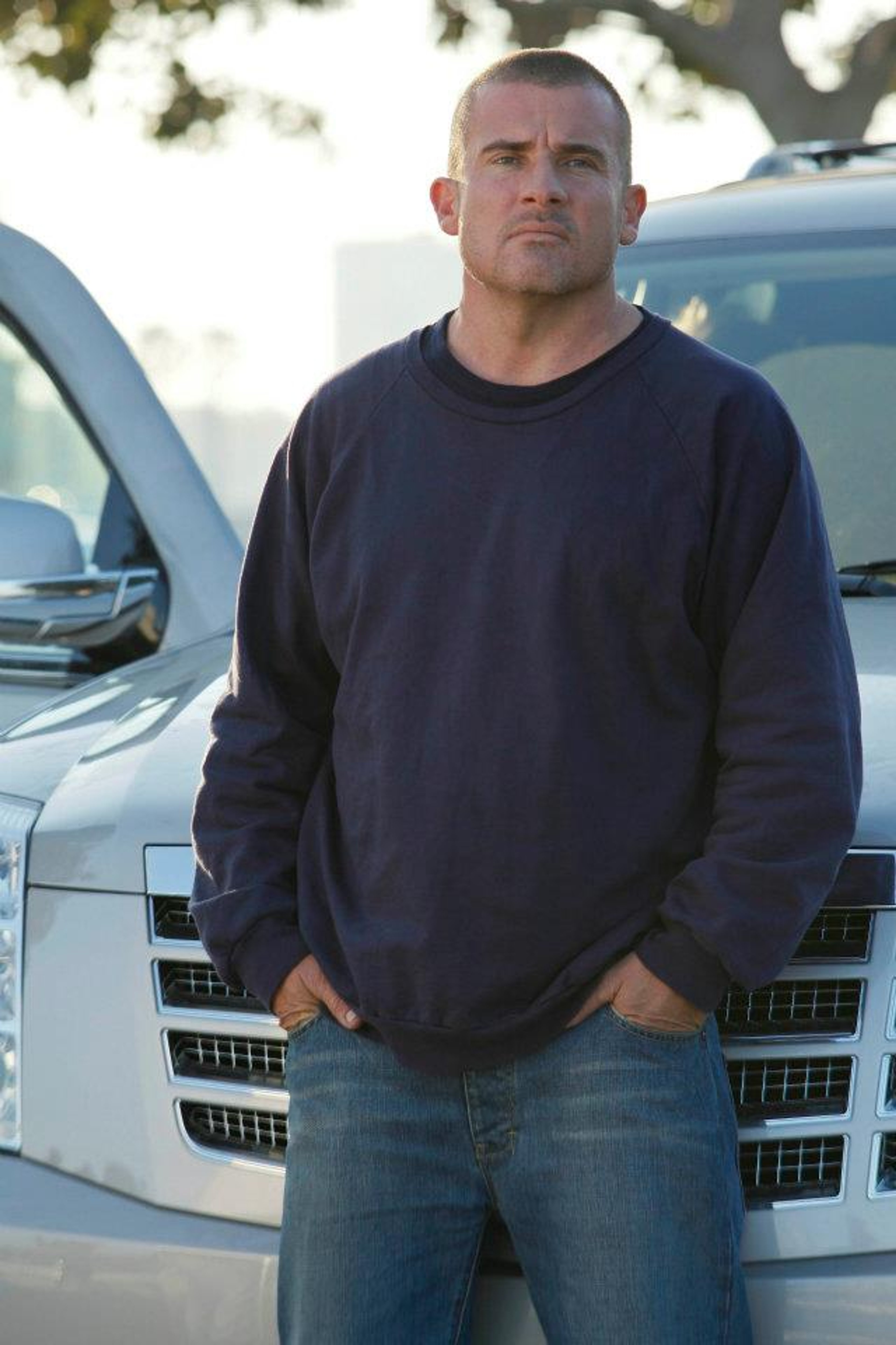 A muscular, bald man in a navy blue shirt standing in front of a vehicle
