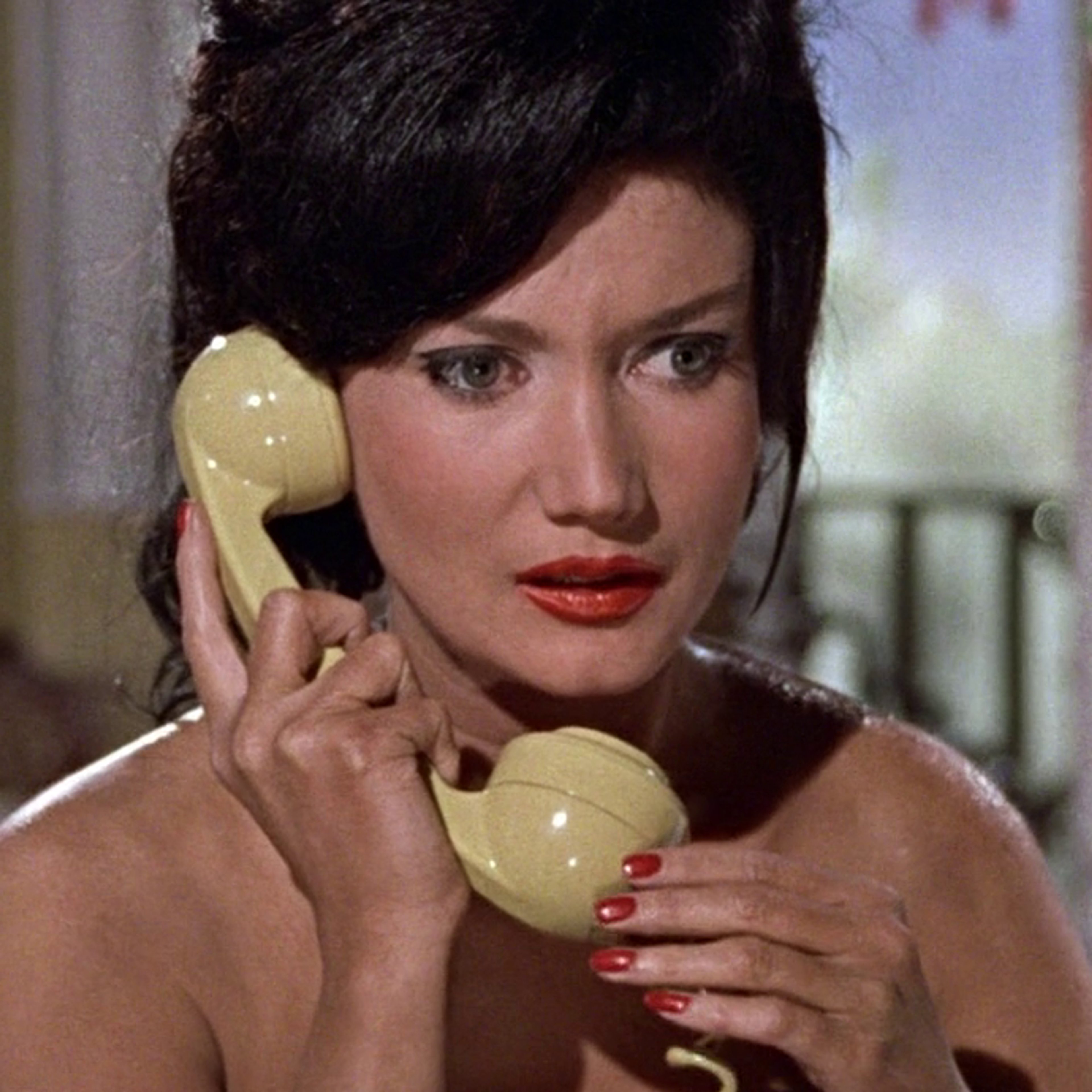 A woman with long dark hair and green eyes holding a telephone receiver