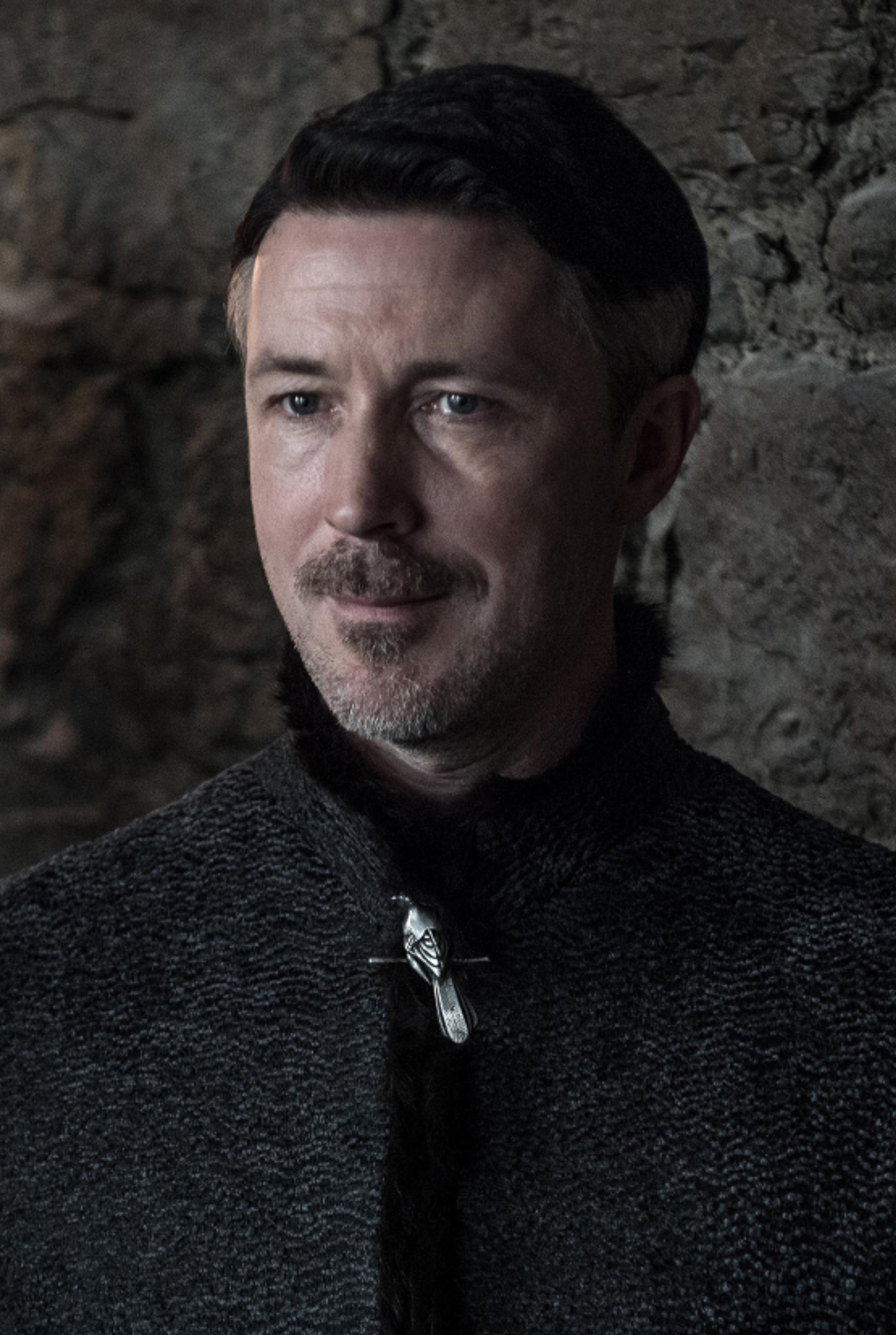 A portrait of a serious-looking middle-aged man with dark hair and a beard, wearing a dark jacket.