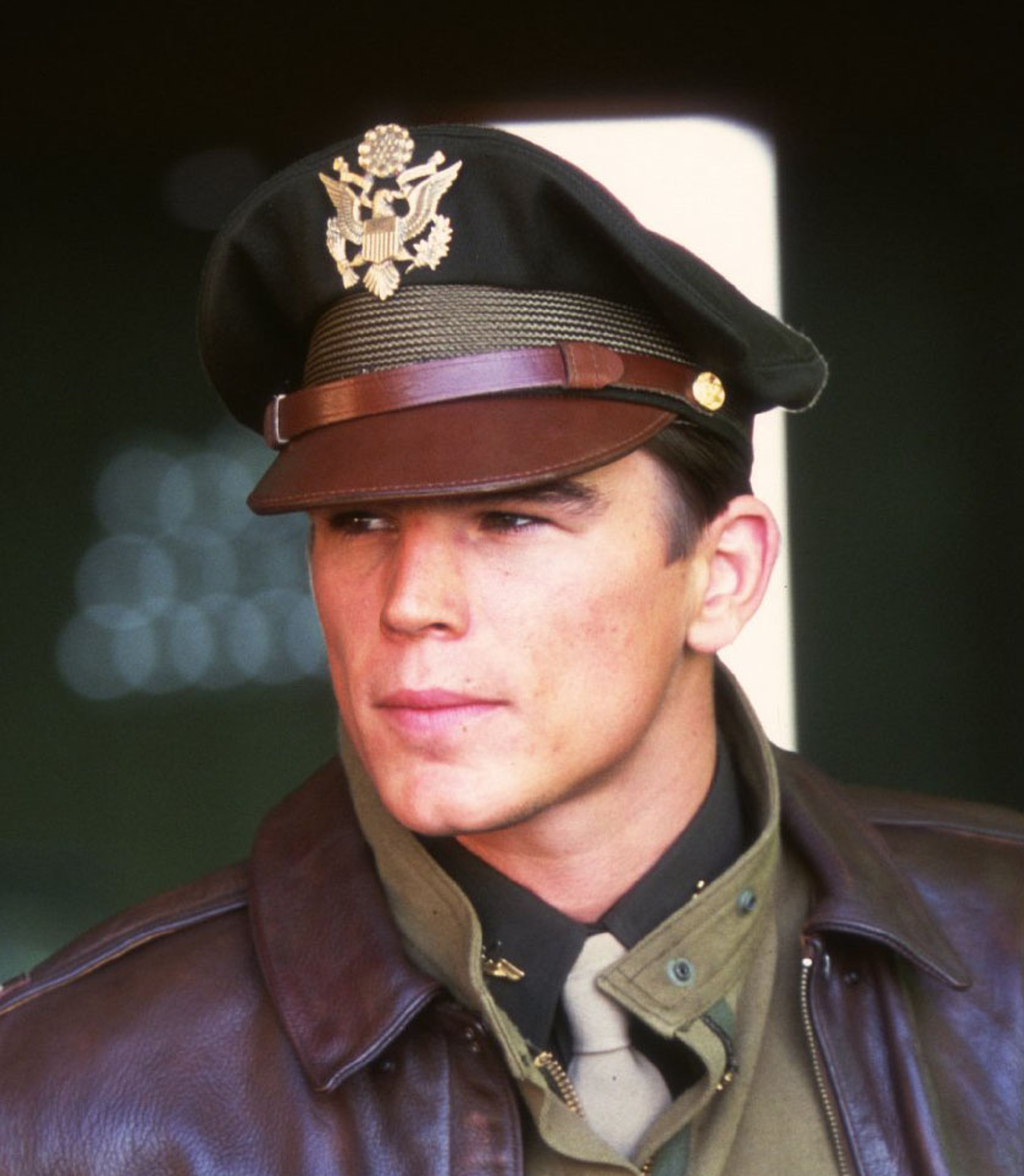 A man in a World War II-era US Army Air Corps captain's uniform, with dark hair and brown eyes.