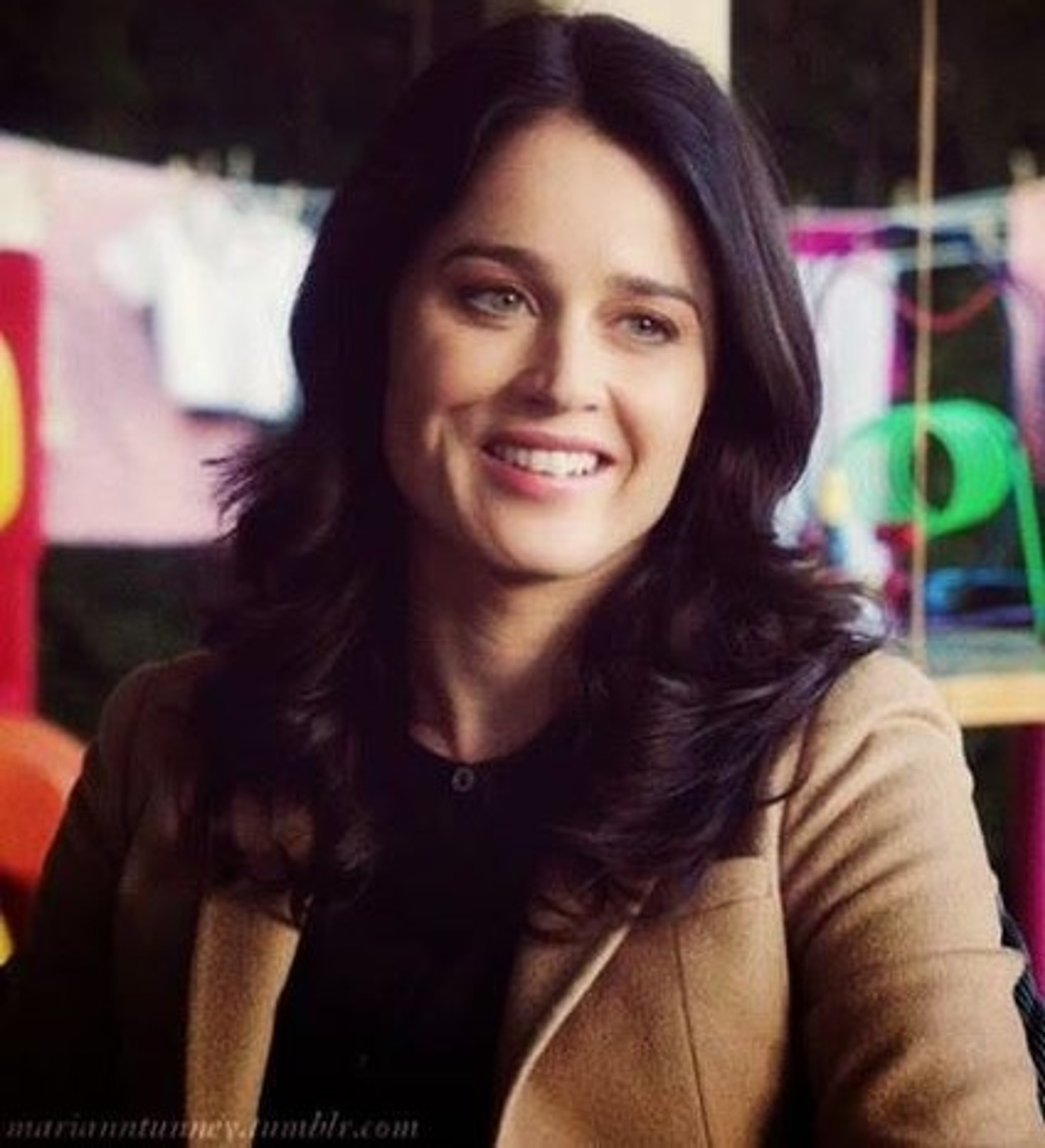 A smiling woman with long dark hair wearing a beige jacket