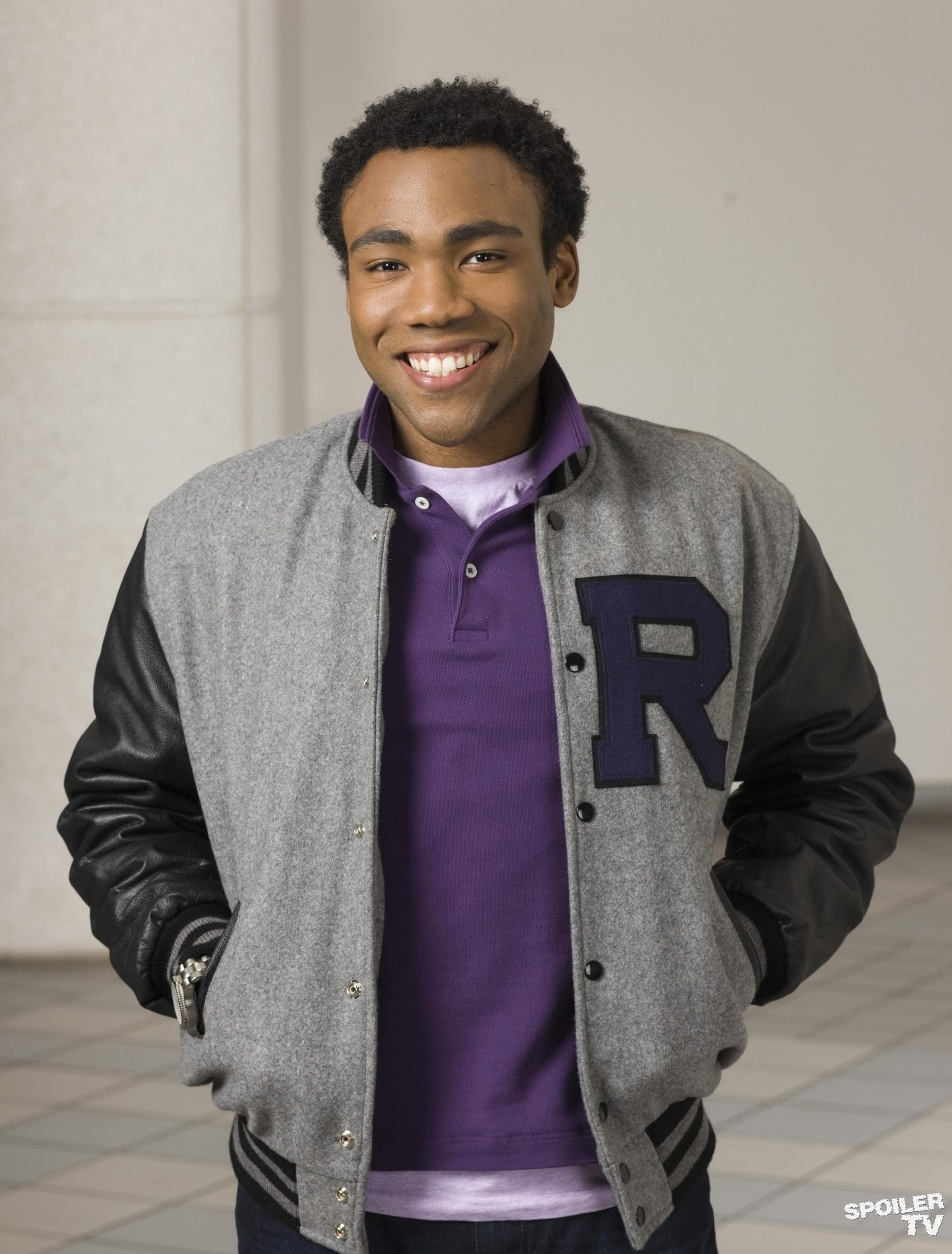 A young Black man with a friendly smile, wearing a gray jacket and purple shirt.