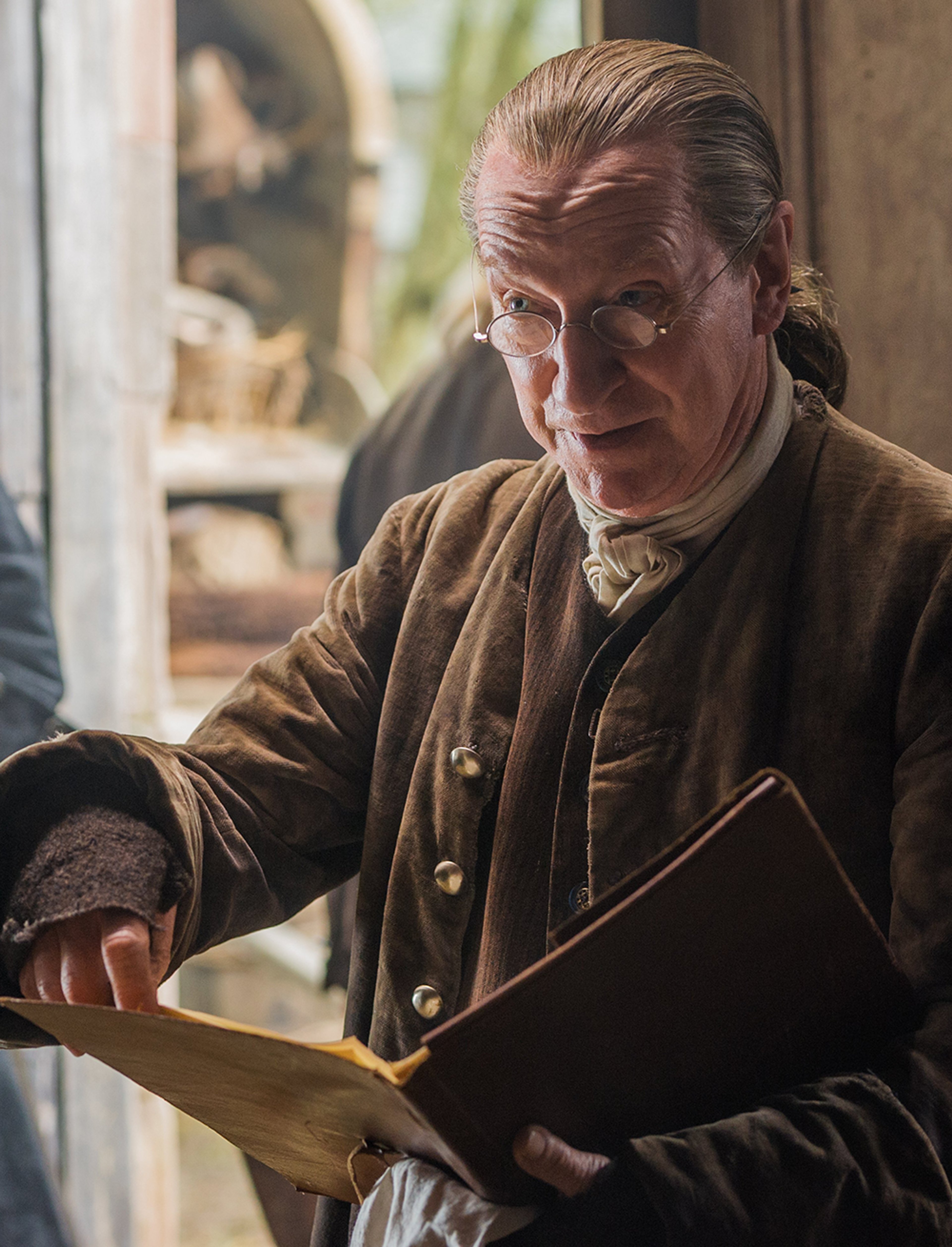 An elderly man in a brown coat holding a book