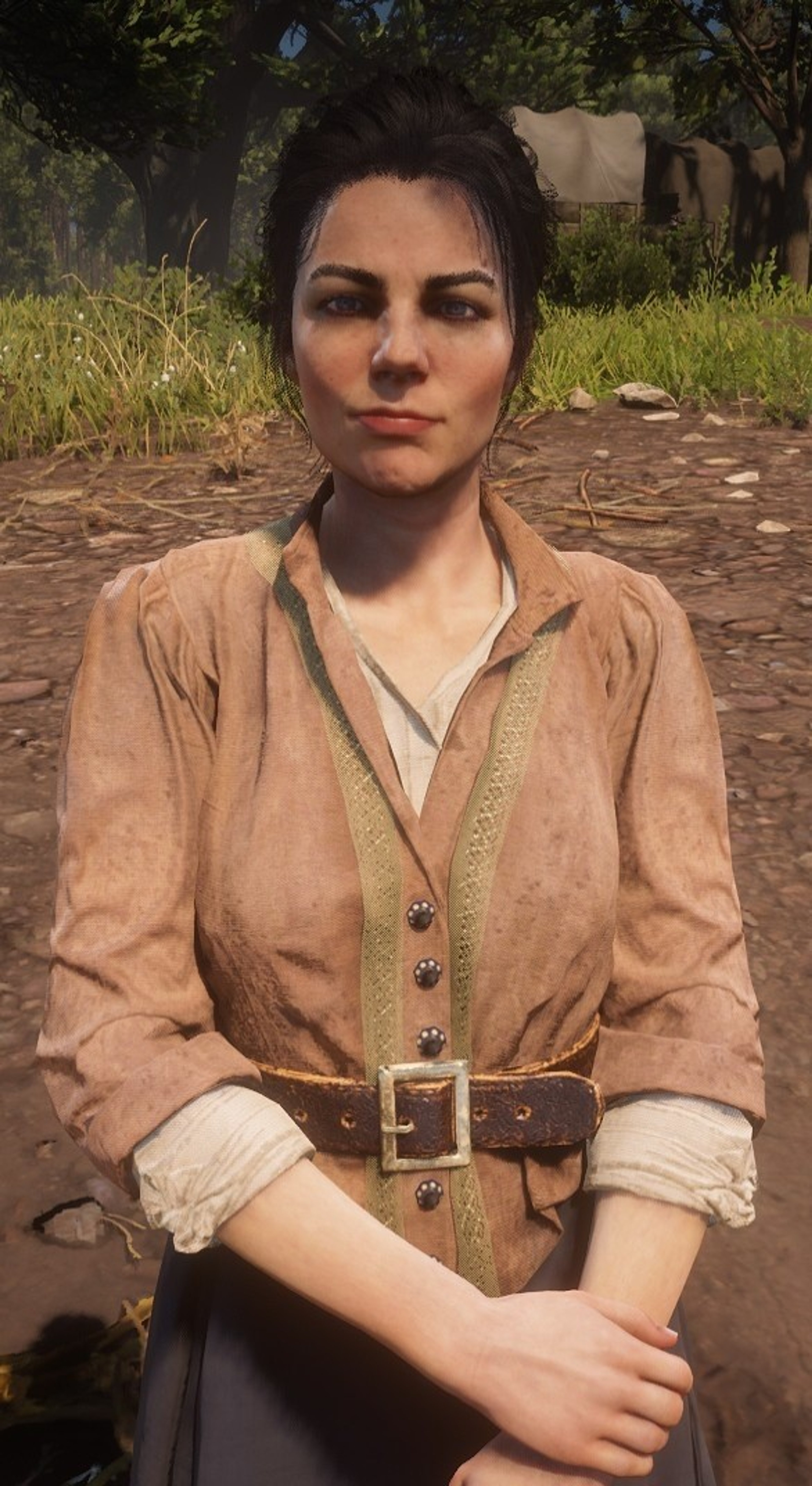 A woman with dark hair wearing a tan shirt or jacket standing in a rural outdoor setting